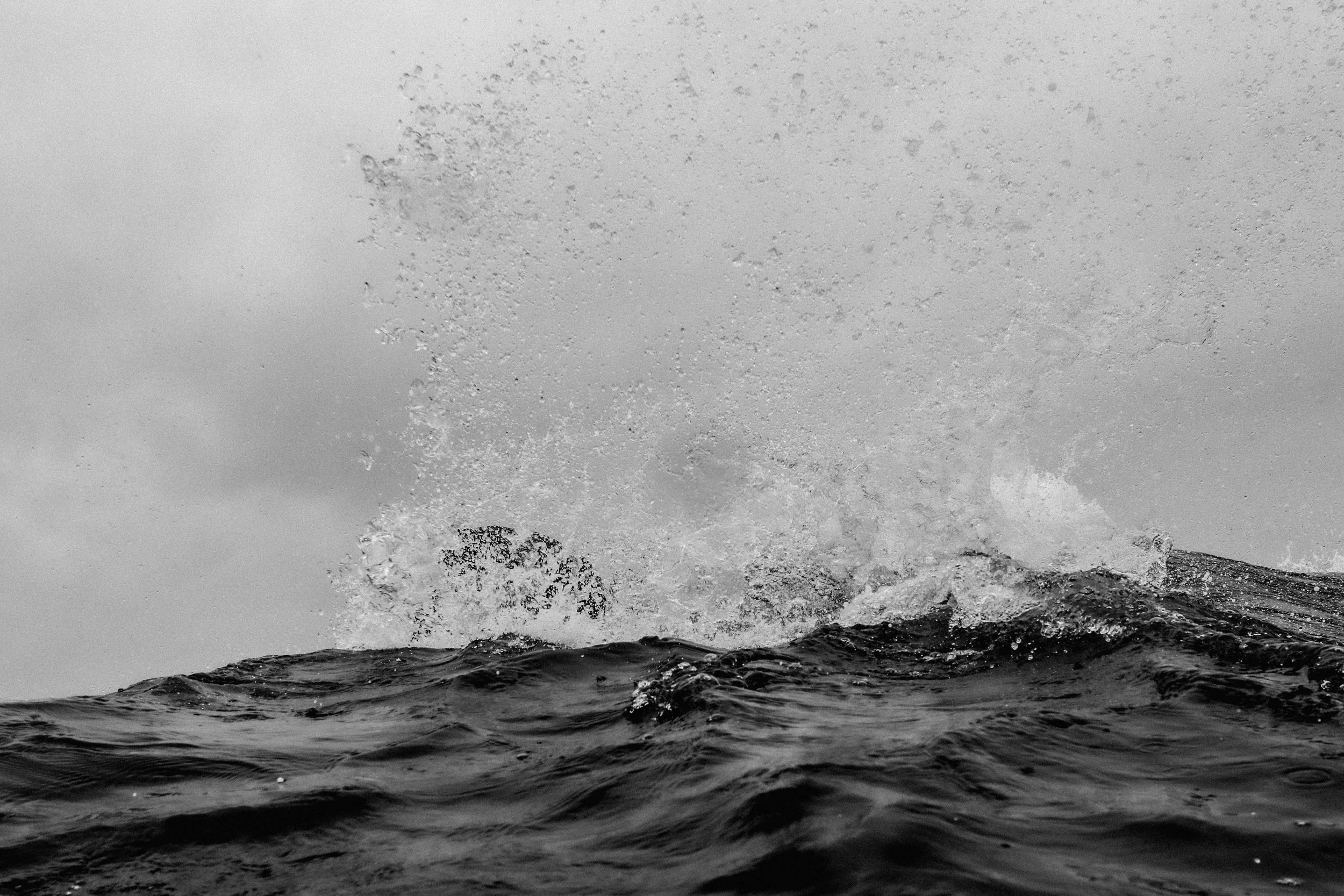A photo of the ocean with waves and water splashing against rocks in black and white.