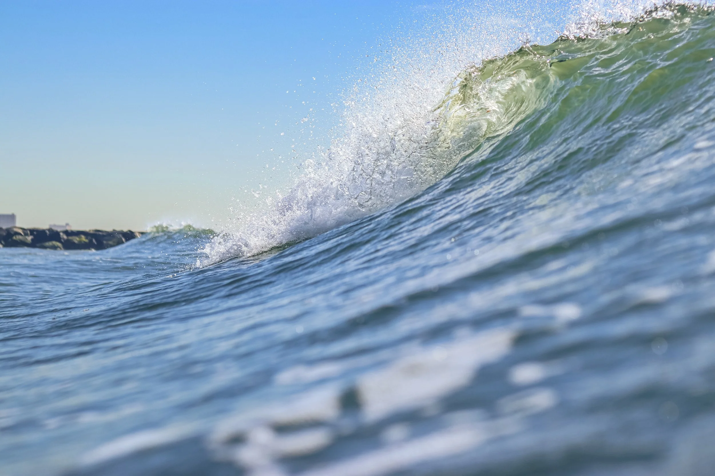 An ocean wave with water spray, under a clear blue sky.