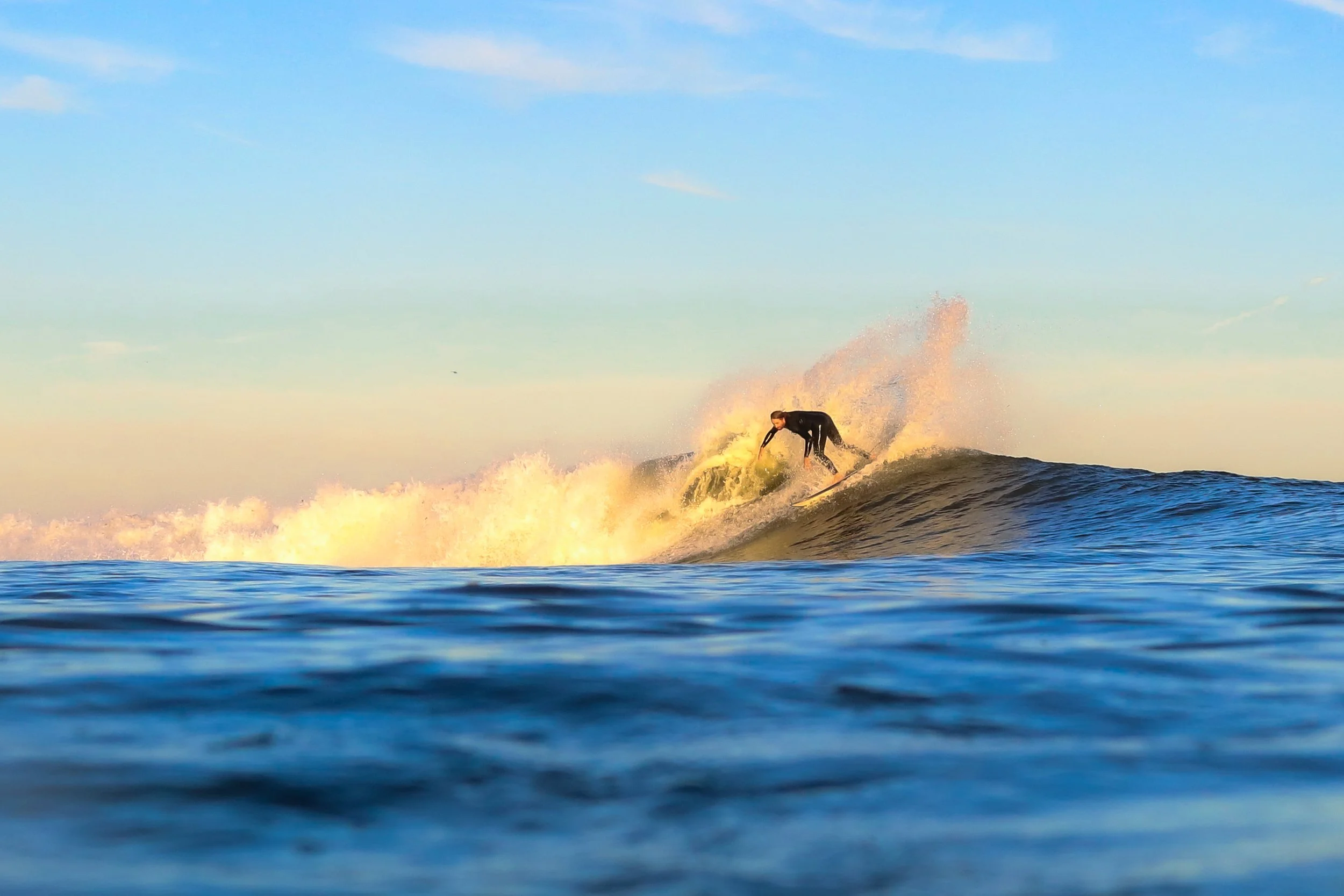 A person surfing on a wave in the ocean with a clear sky in the background.