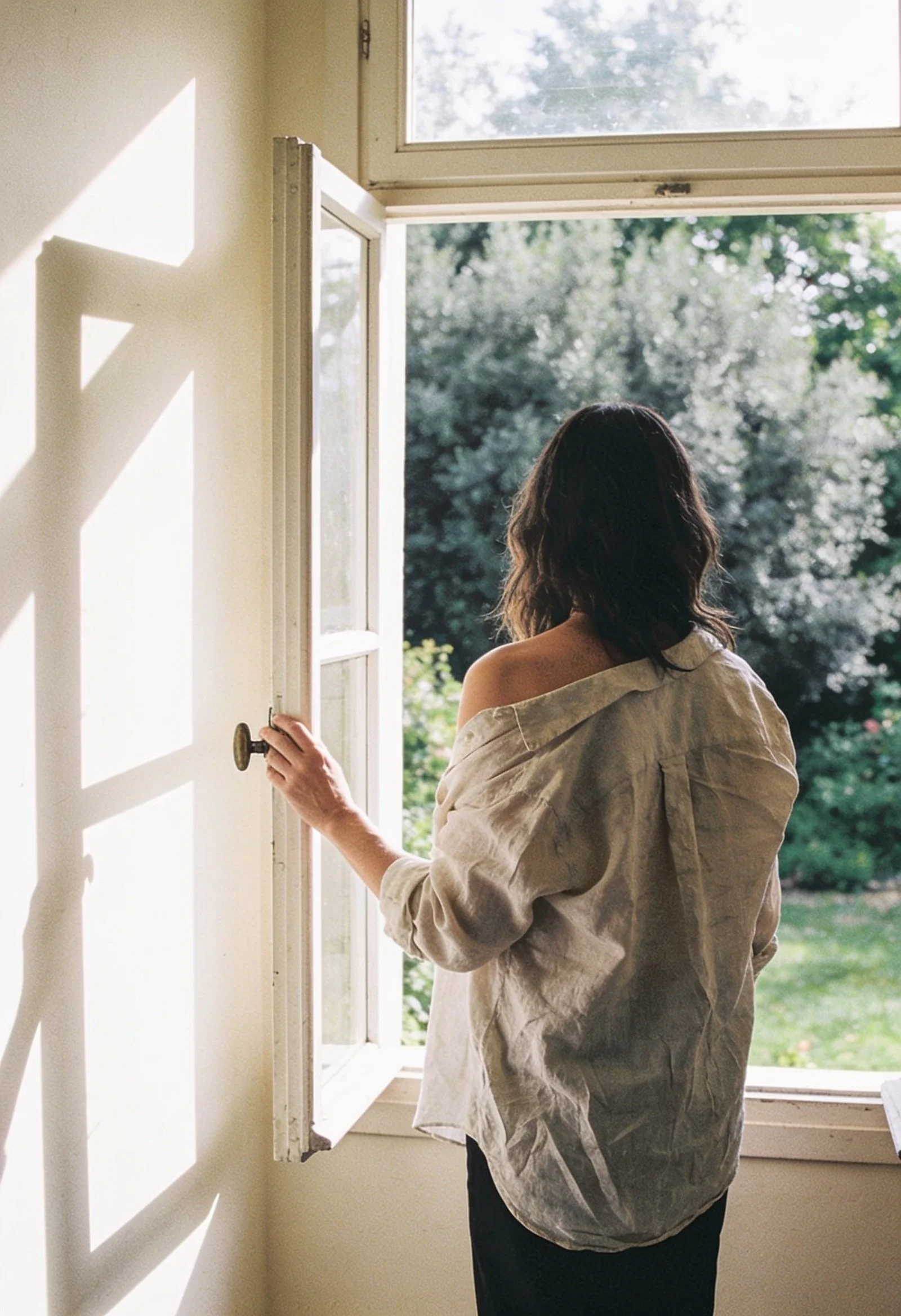Femme de dos qui ouvre une fenêtre sur un jardin, lumière franche, écouter ses émotions plutôt que les gérer