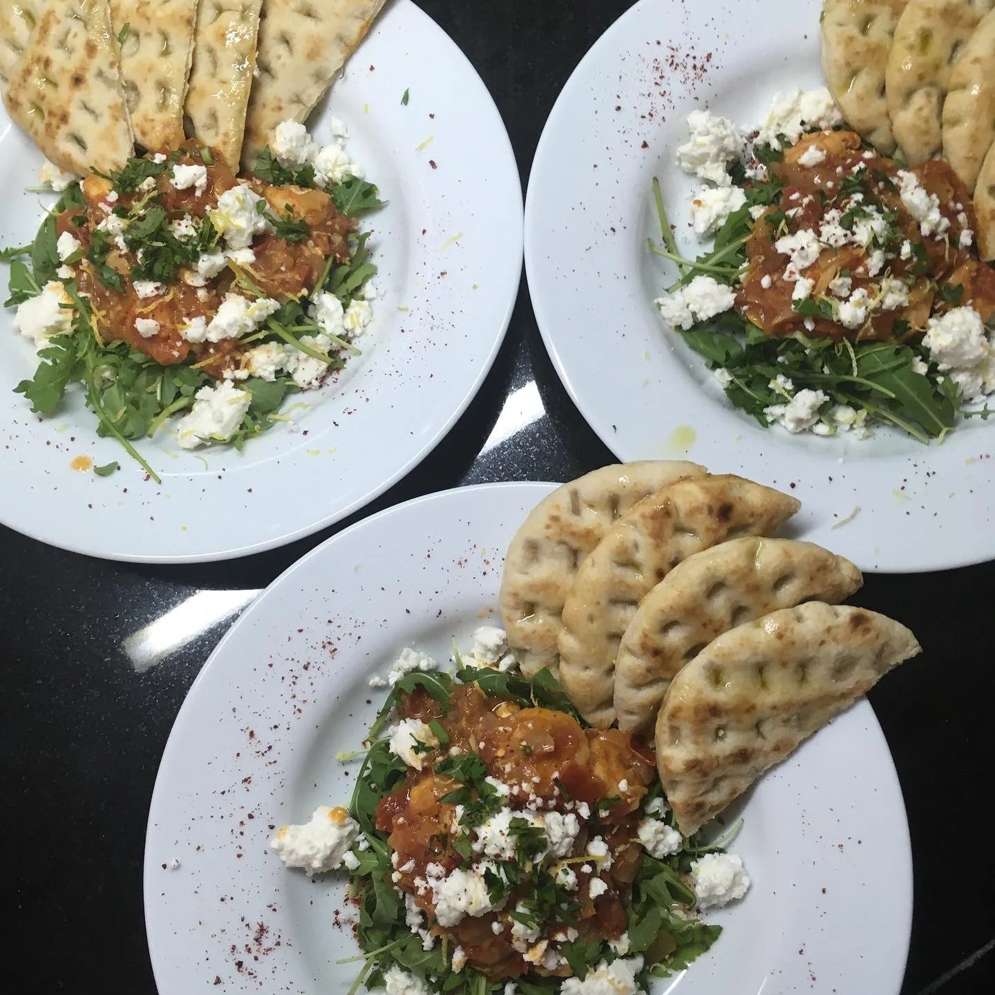 Three plates of salad with crumbled cheese and grilled flatbread.