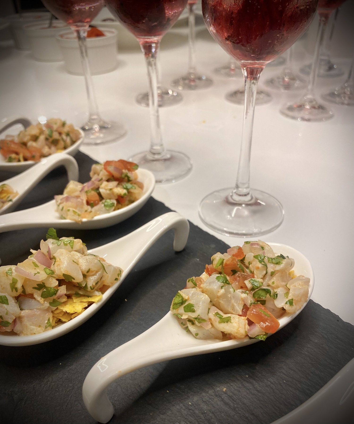 White ceramic spoons of seafood salad on a black slate platter.