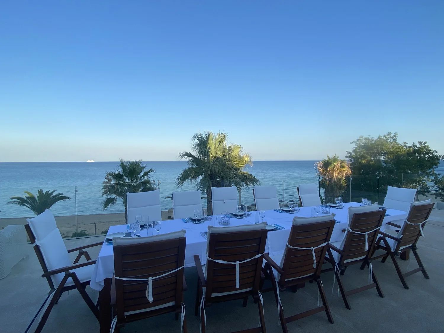 Outdoor dining table set in white linen, overlooking the sea.
