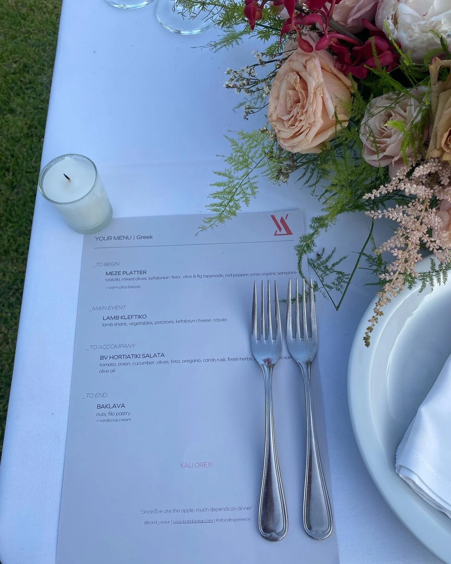 Table setting with candle, printed menu, peach and pink florals.