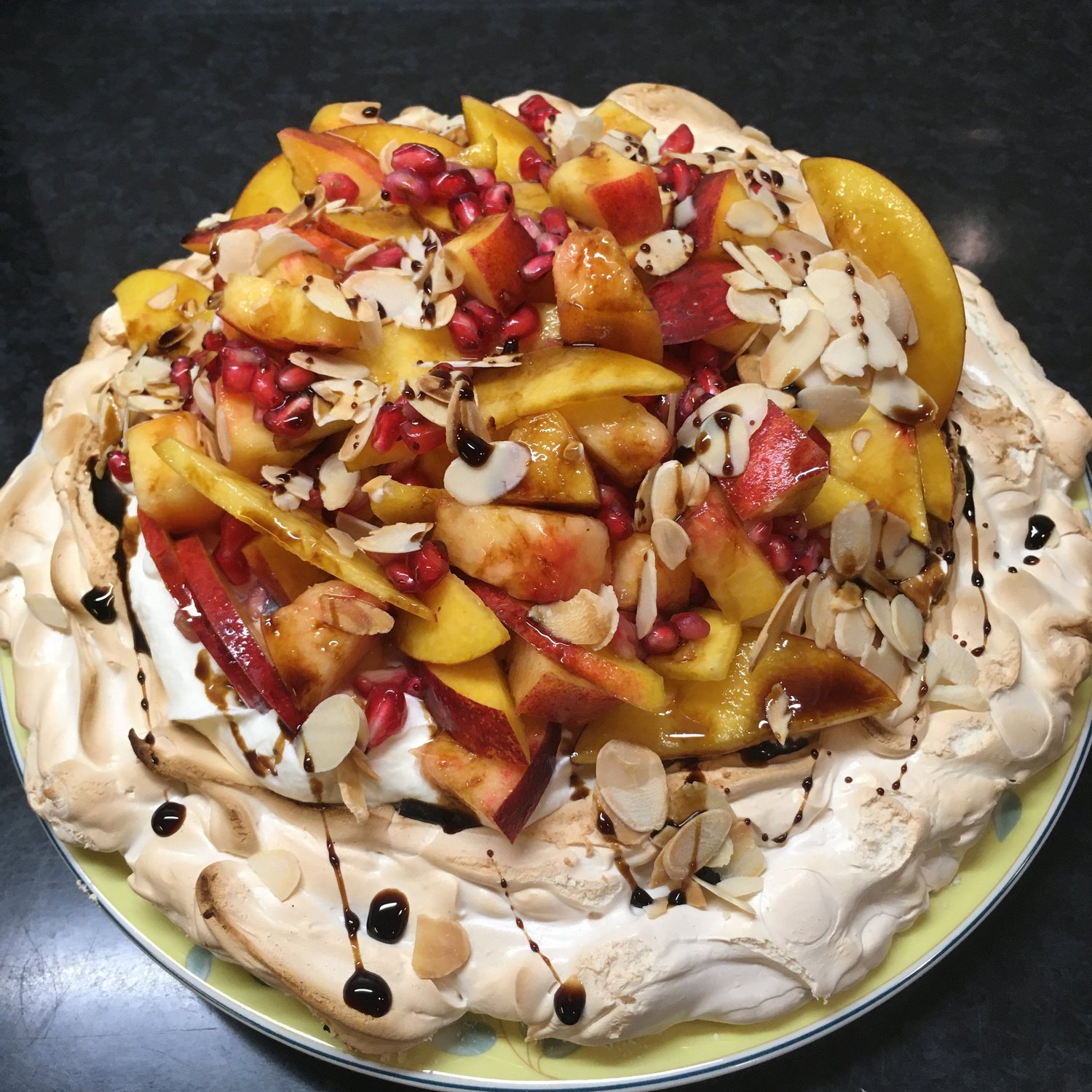 Pavlova with whipped cream, fruit, pomegranate and almonds.