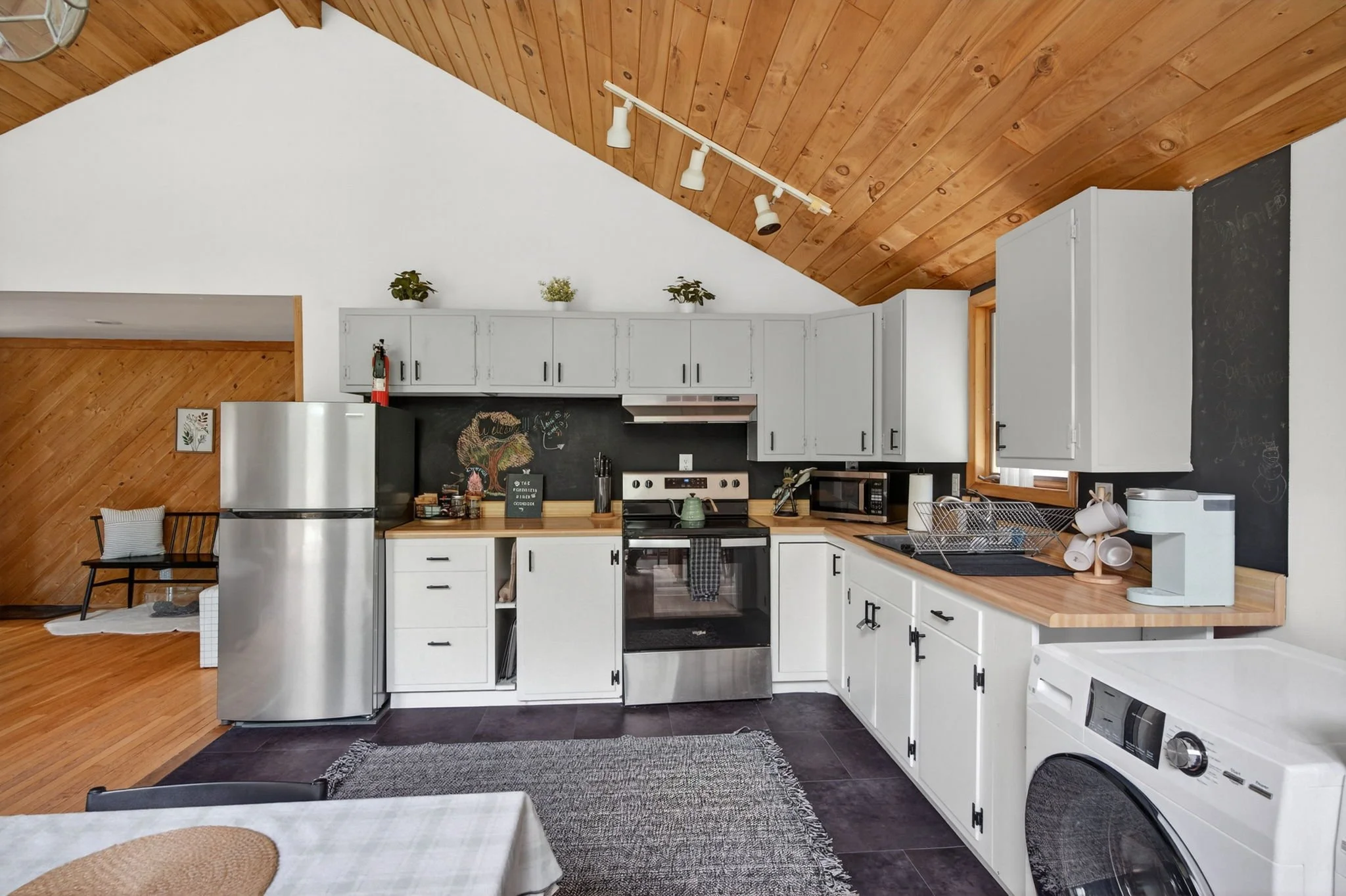 Kitchen with white cabinets, wooden countertops, stainless steel appliances, black chalkboard wall, and wood-paneled ceiling.