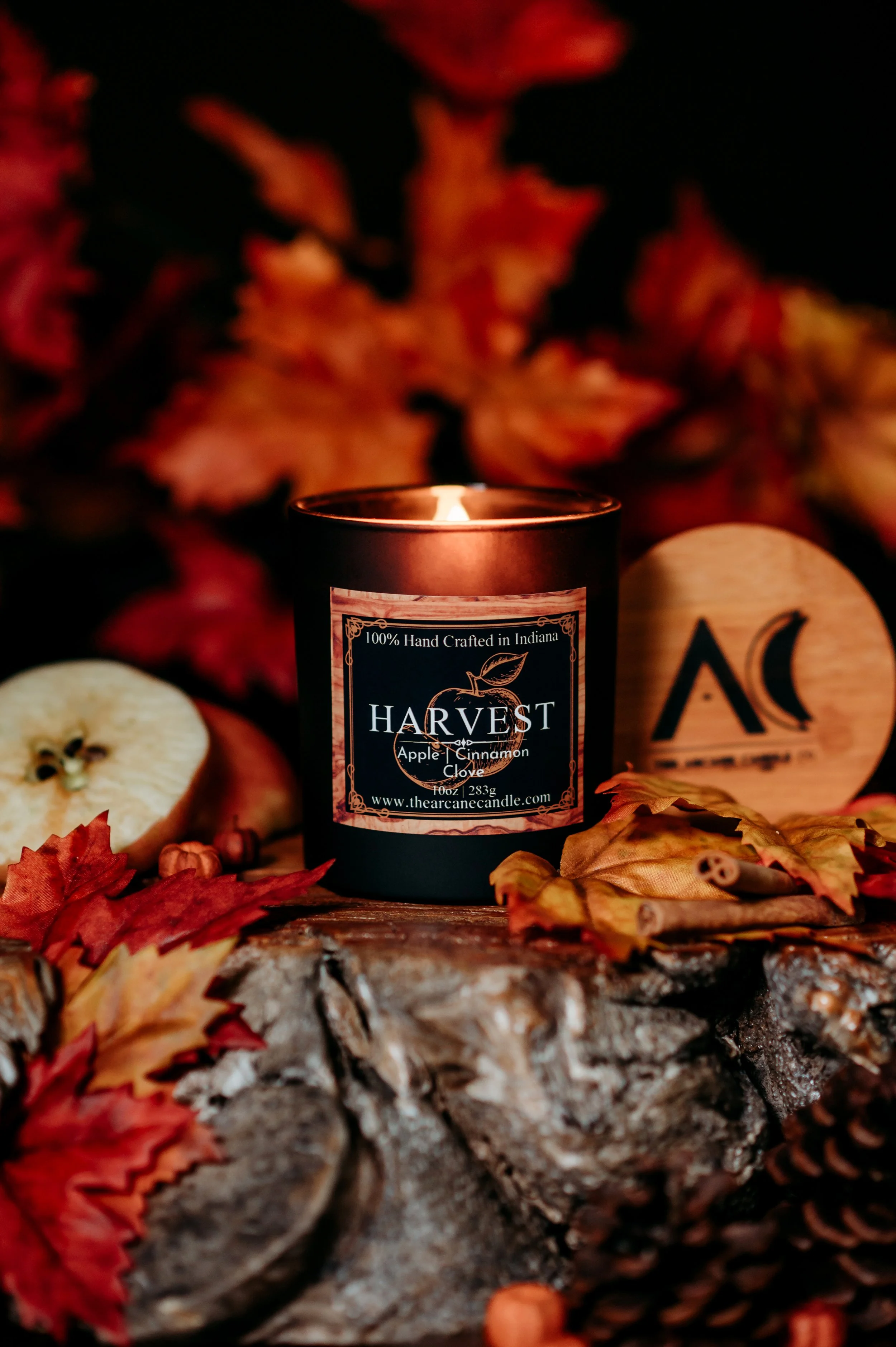 HARVEST apple cinnamon candle glowing in a rustic autumn display with colorful leaves, apples and warm spices.