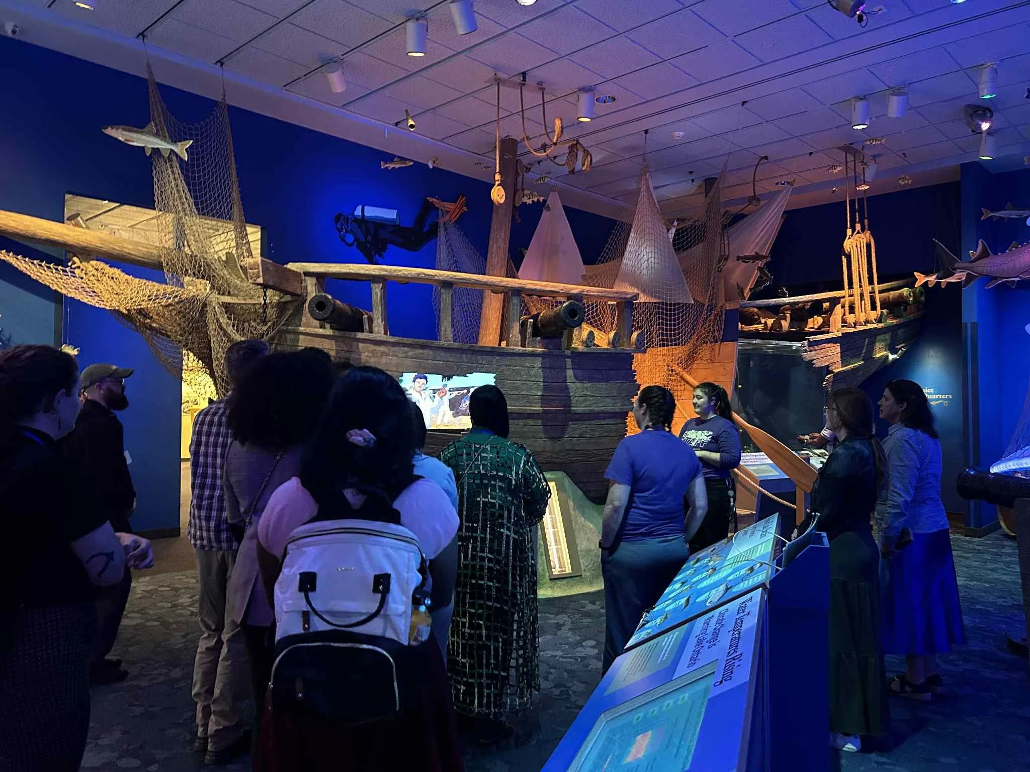 alt="a group of people look at a large scale replica of a shipwreck in a museum."