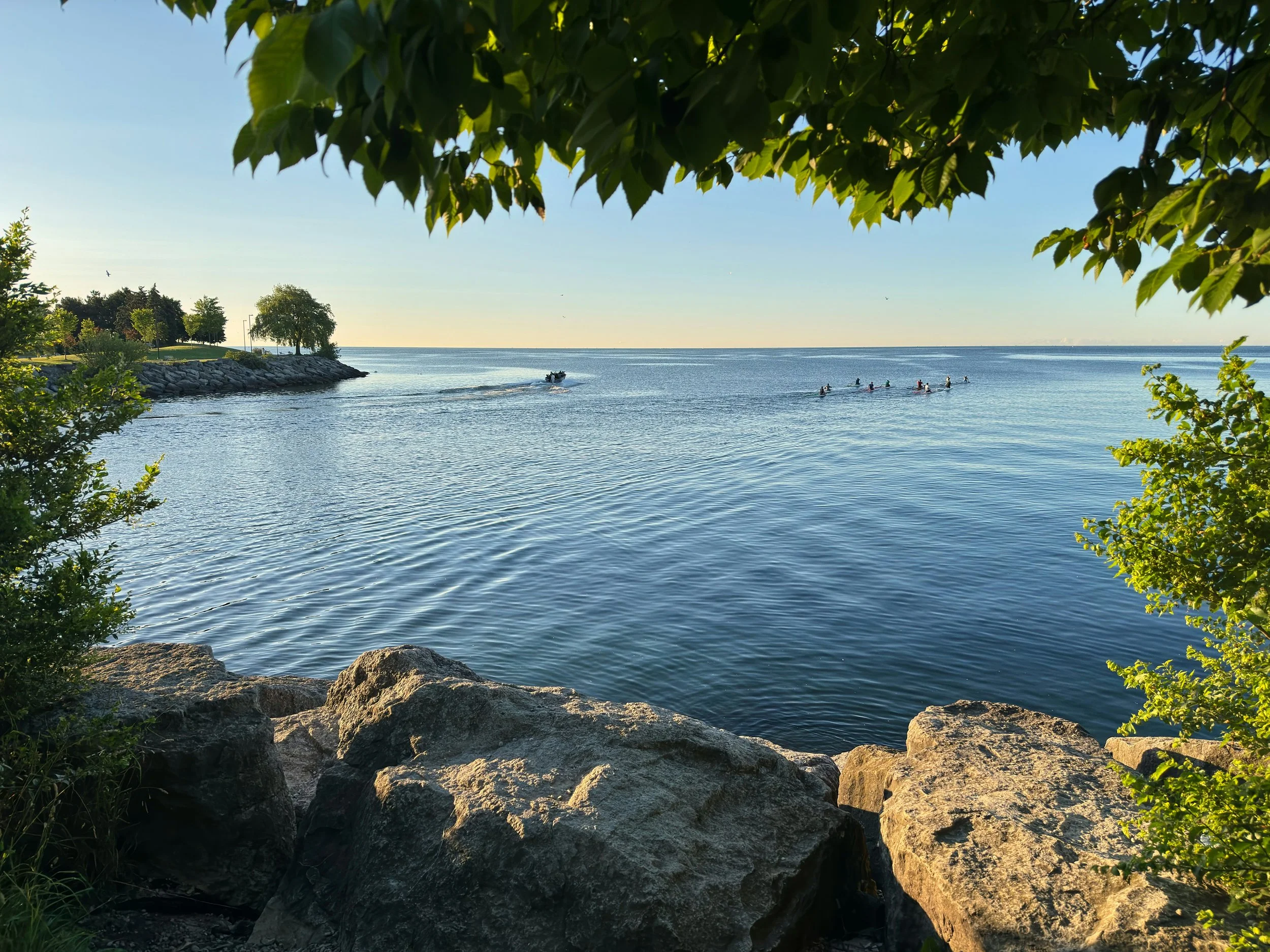 sunrise on a lake with a rocky shoreline and trees with paddlers in the background