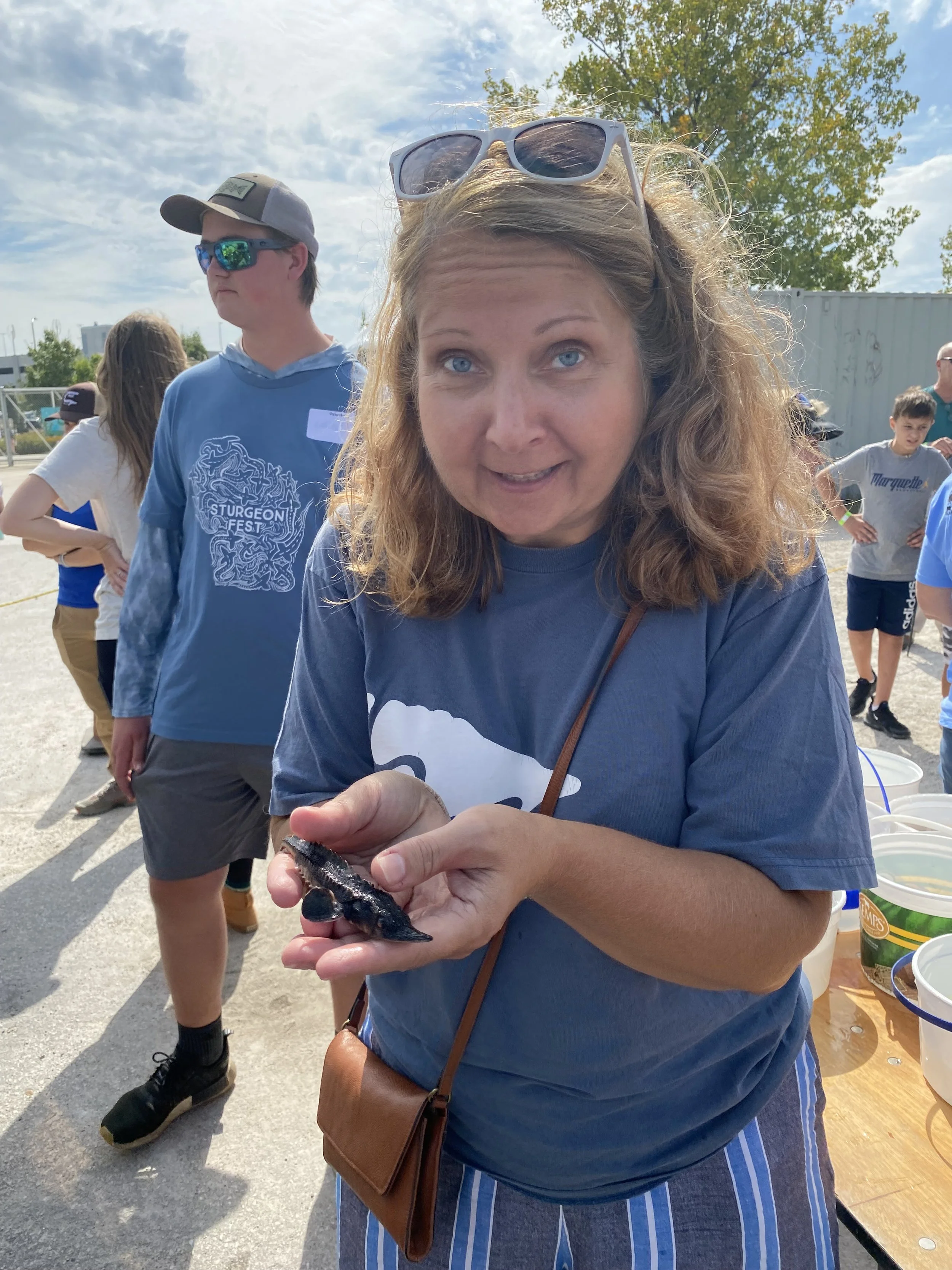 a middle-aged white woman holds a baby sturgeon in her hands while smiling