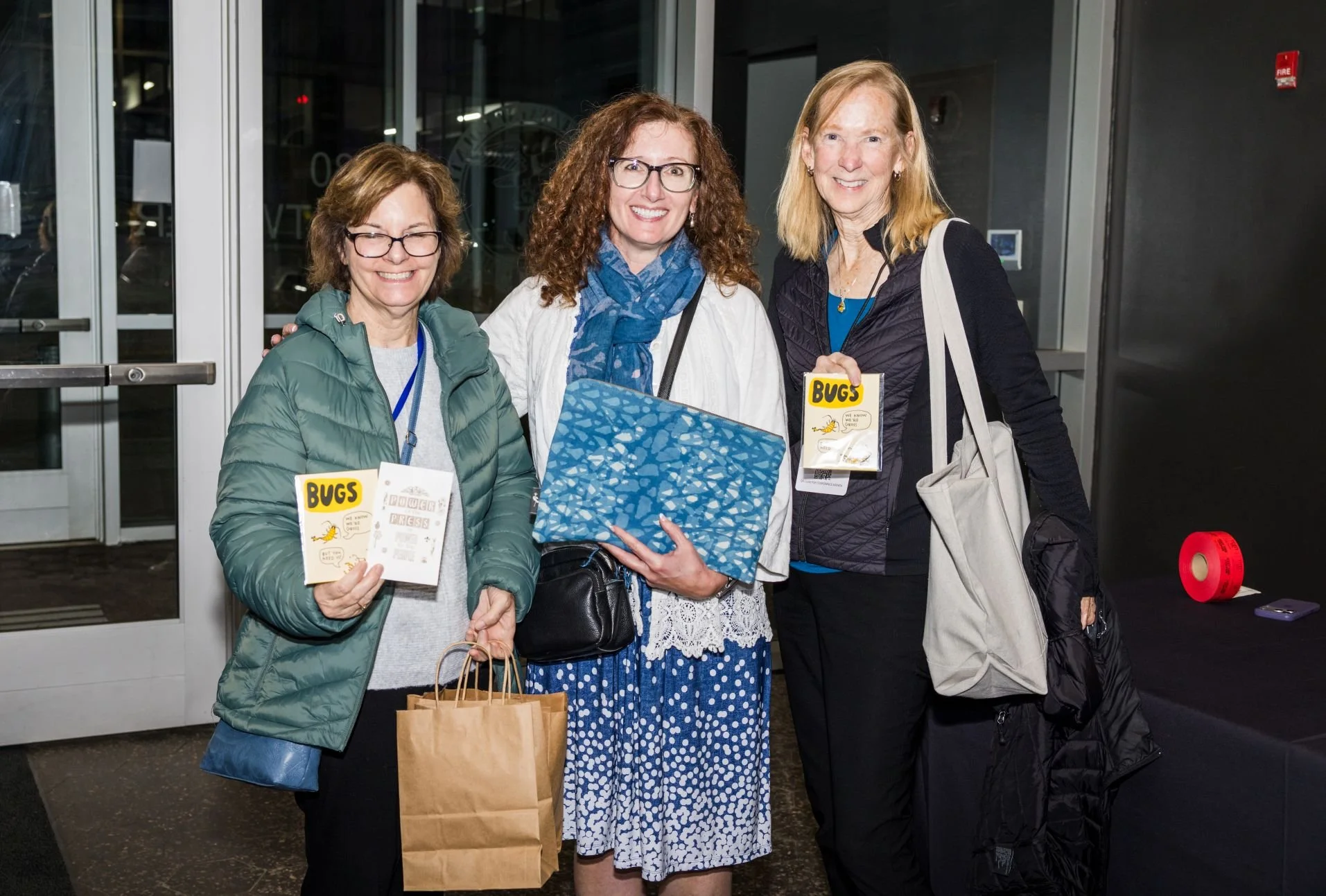 Three smiling people stand with purchases of zines and a scarf.