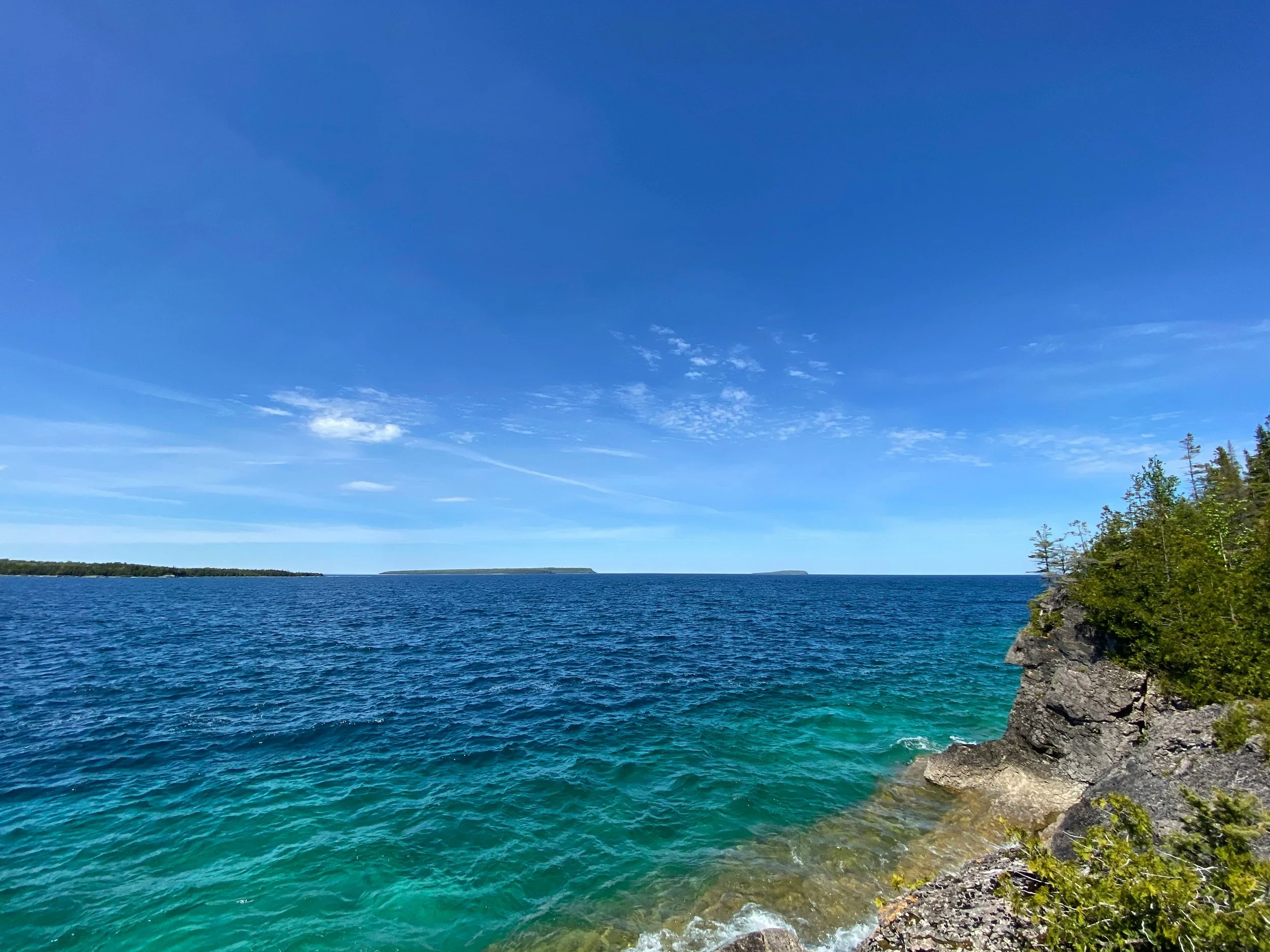 a sunny day on a clear blue lake with a rocky shoreline