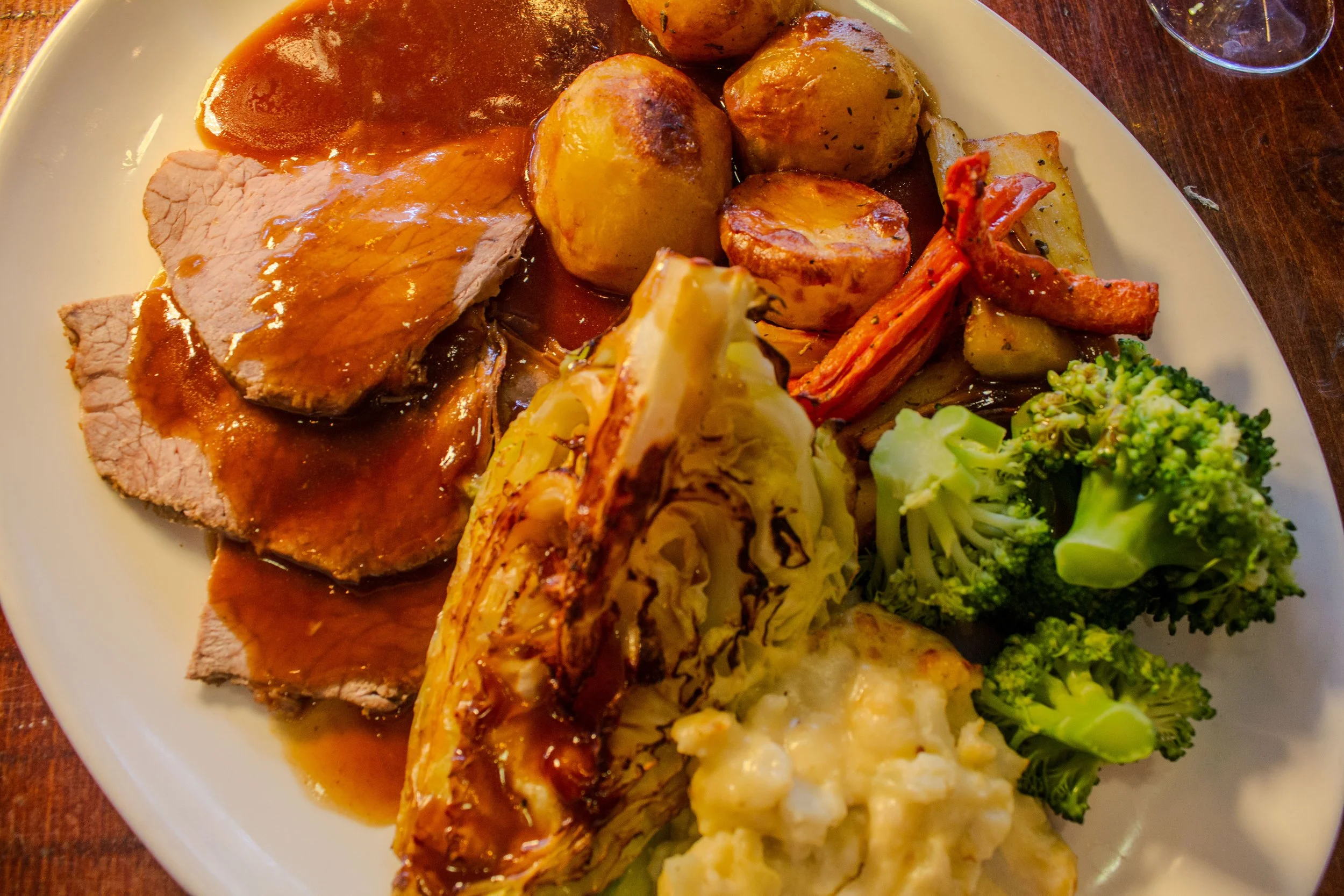 A white plate of food featuring sliced roast beef with gravy, roasted potatoes, a roasted carrot, broccoli, and mashed potatoes.