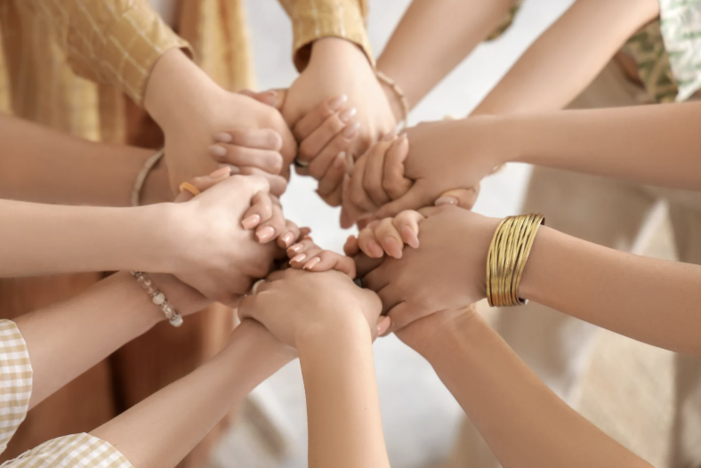 Multiple hands of children and adults stacked together in a circle, symbolizing unity and teamwork.