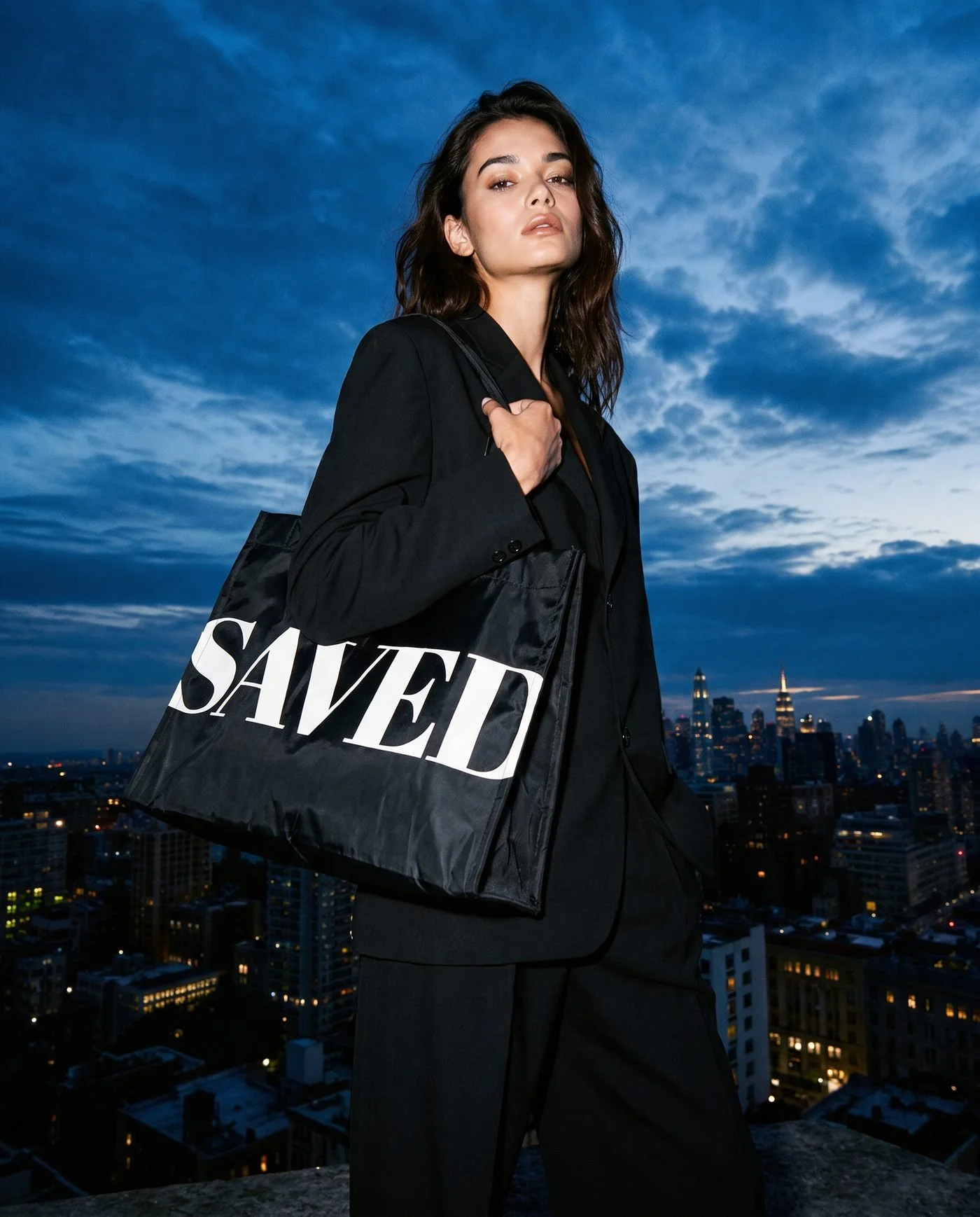 Woman on a city rooftop at dusk carrying the SAVED tote