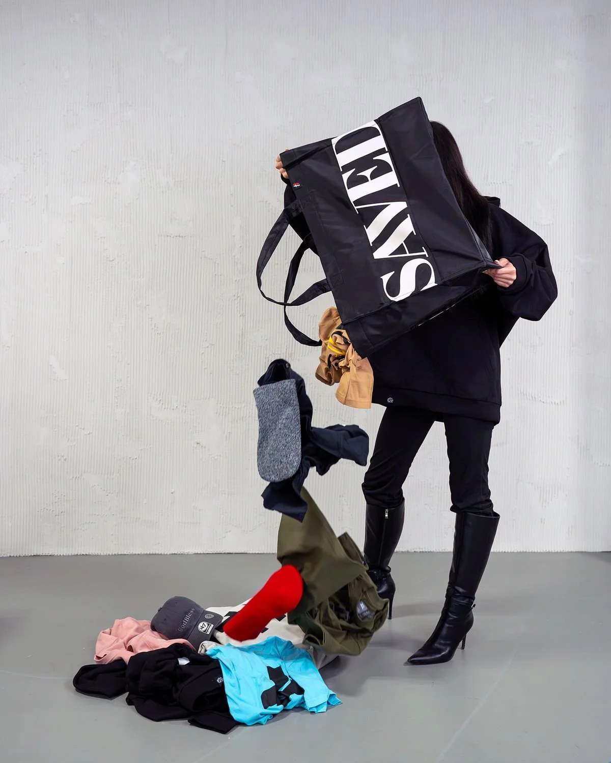 Woman tipping a black SAVED tote full of Hashtag God clothing onto the floor