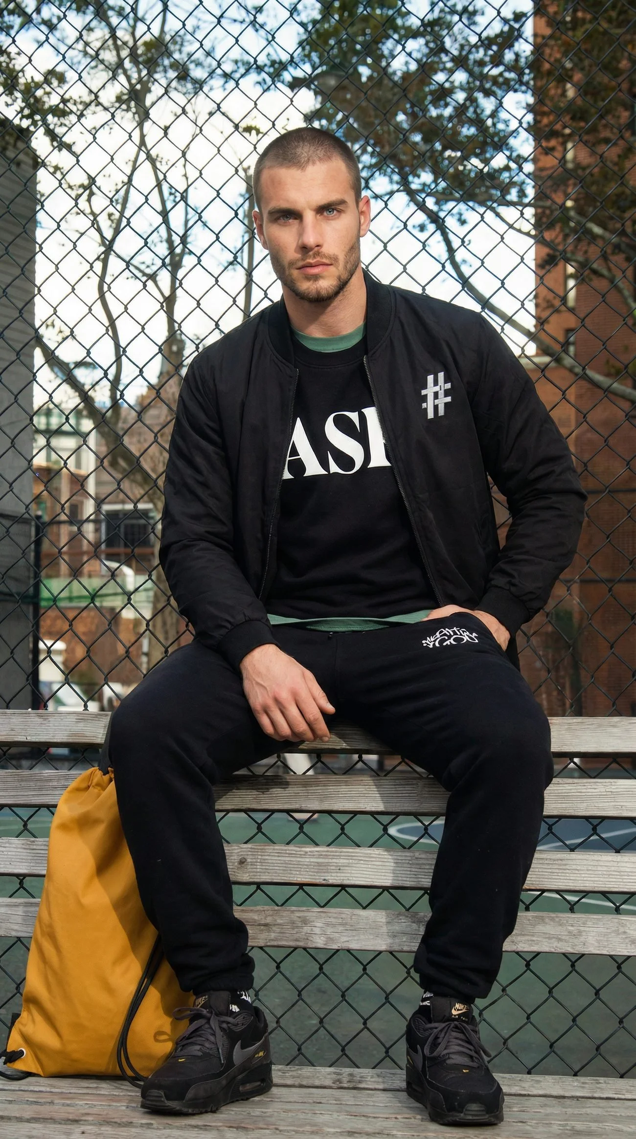 Man in a black # bomber and ASK crewneck on a courtside bench