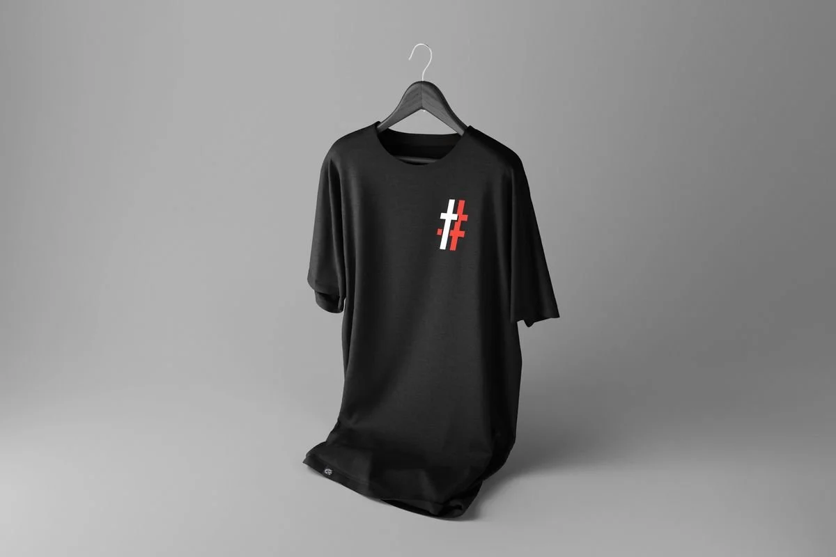 Black tee with a small red and white # cross mark on the chest