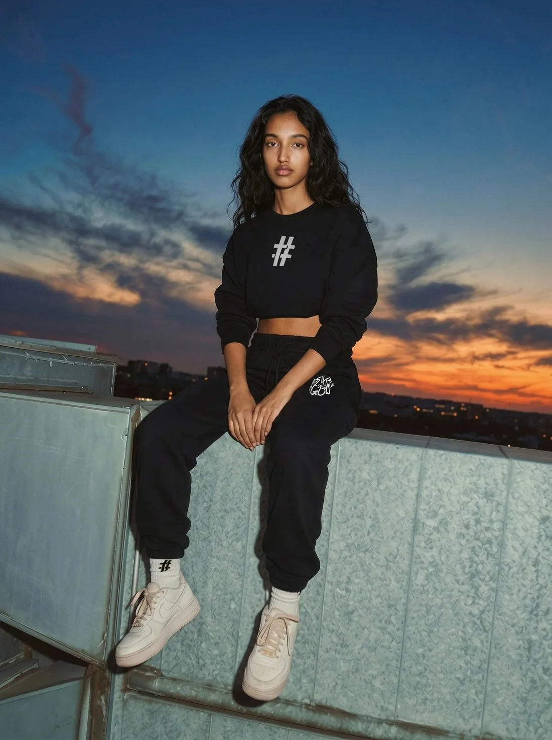 Woman in a black # cropped crewneck and sweats on a rooftop at sunset