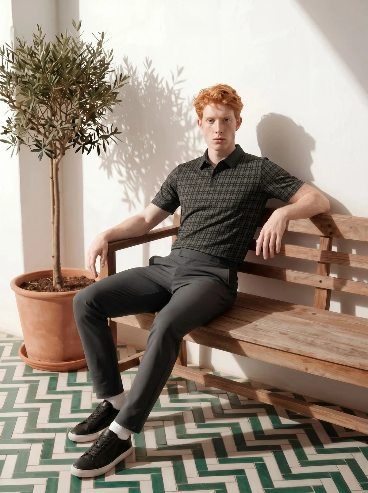 Man in the Believe polo on a wooden bench beside an olive tree