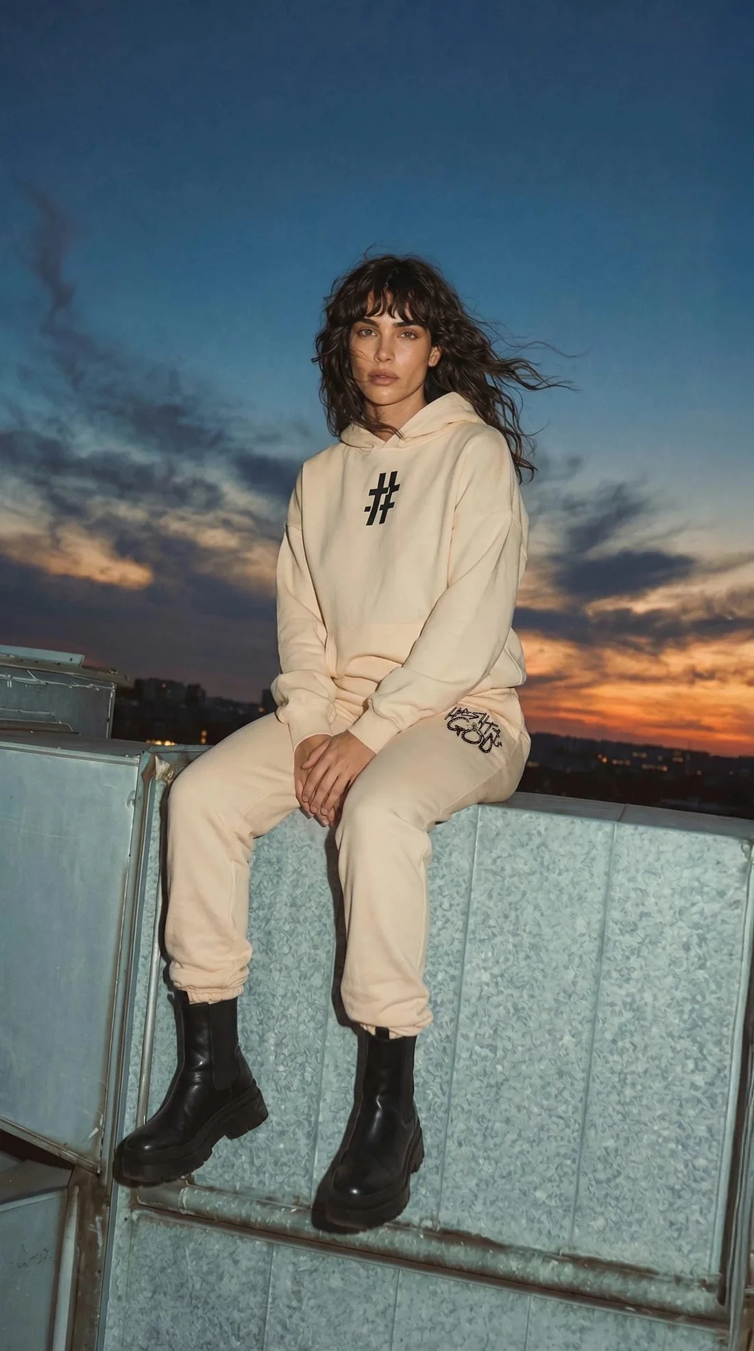 Woman in a cream # hoodie and sweats on a rooftop at sunset