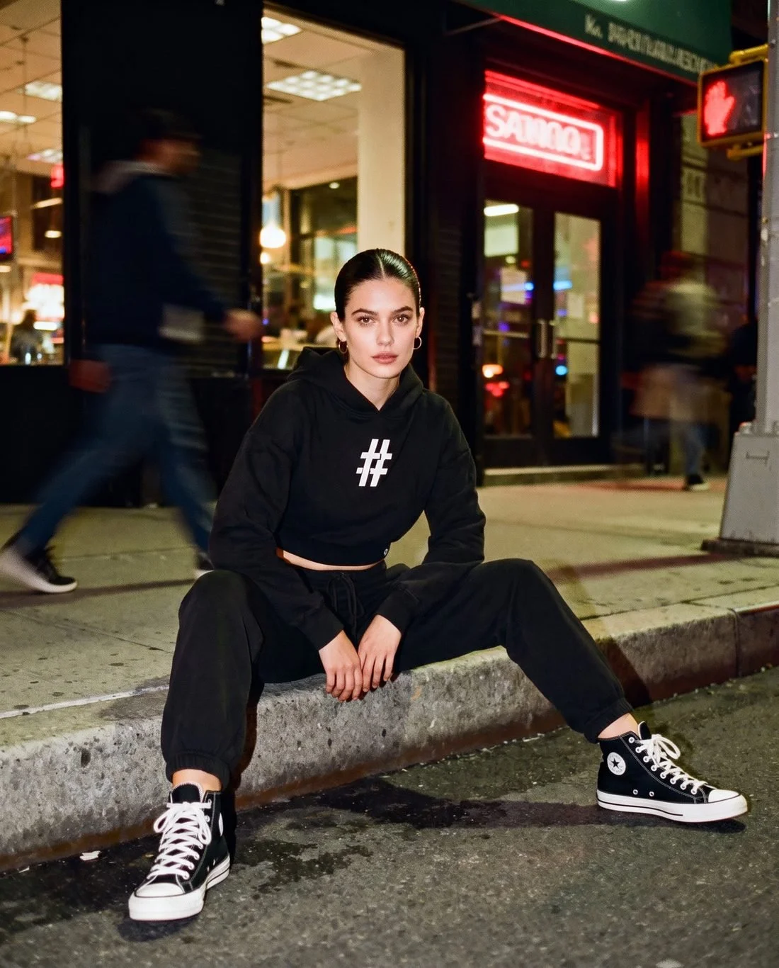 Woman in a black # cropped hoodie sitting on a city curb at night
