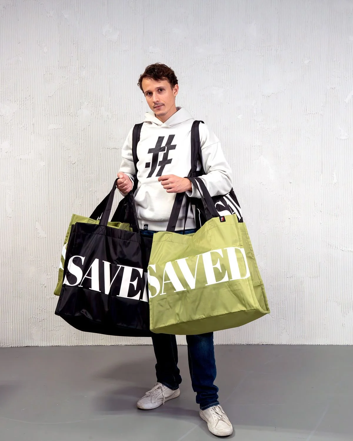 Man in a cream # hoodie carrying black and olive SAVED bags