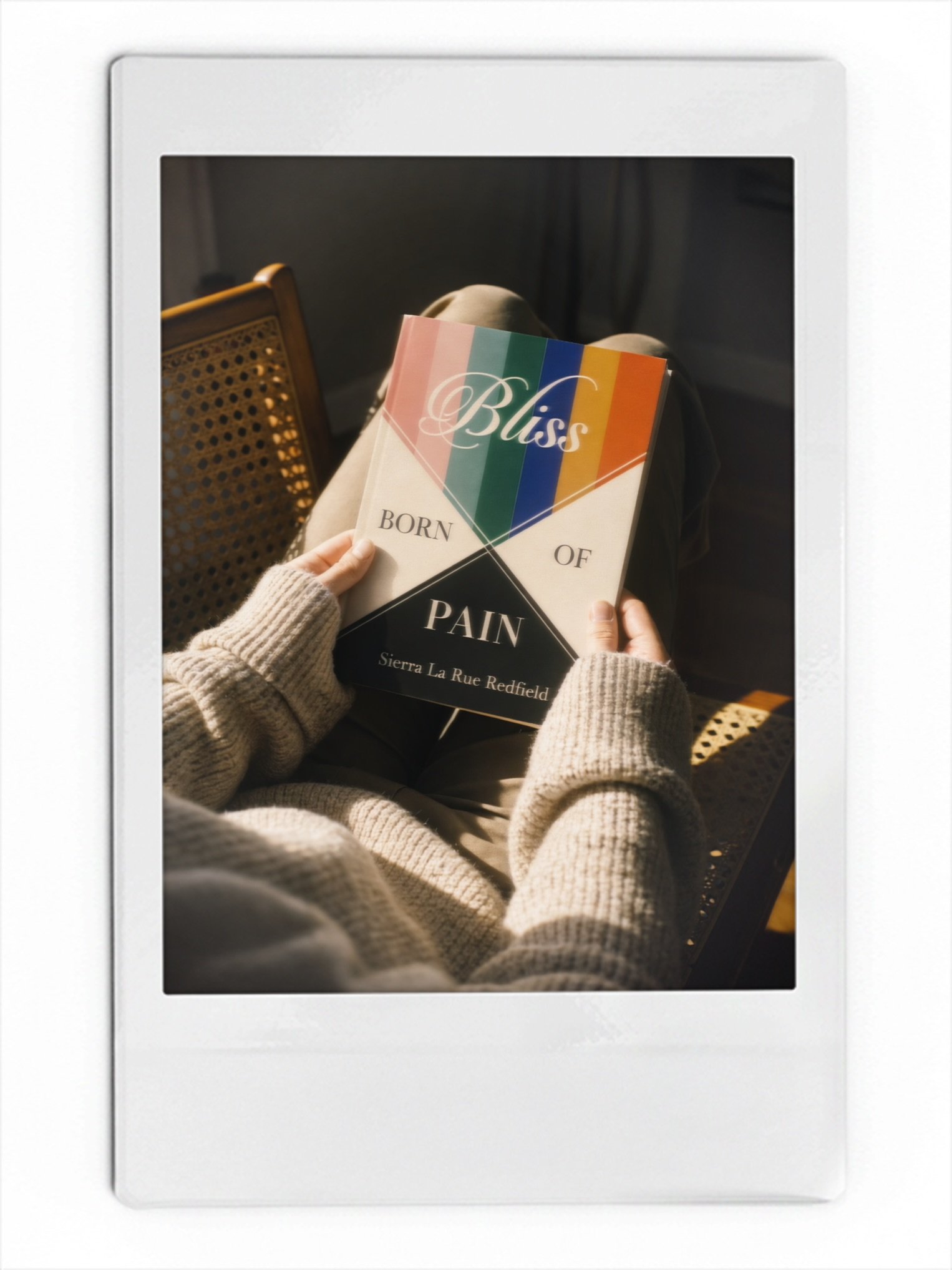 Reader holding Bliss Born of Pain by Sierra La Rue Redfield while seated in a chair.