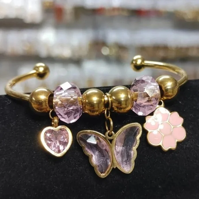 Pulsera rosa con mariposa, corazón y flor en acero inoxidable. Pink bracelet with butterfly, heart, and flower charms in stainless steel.
