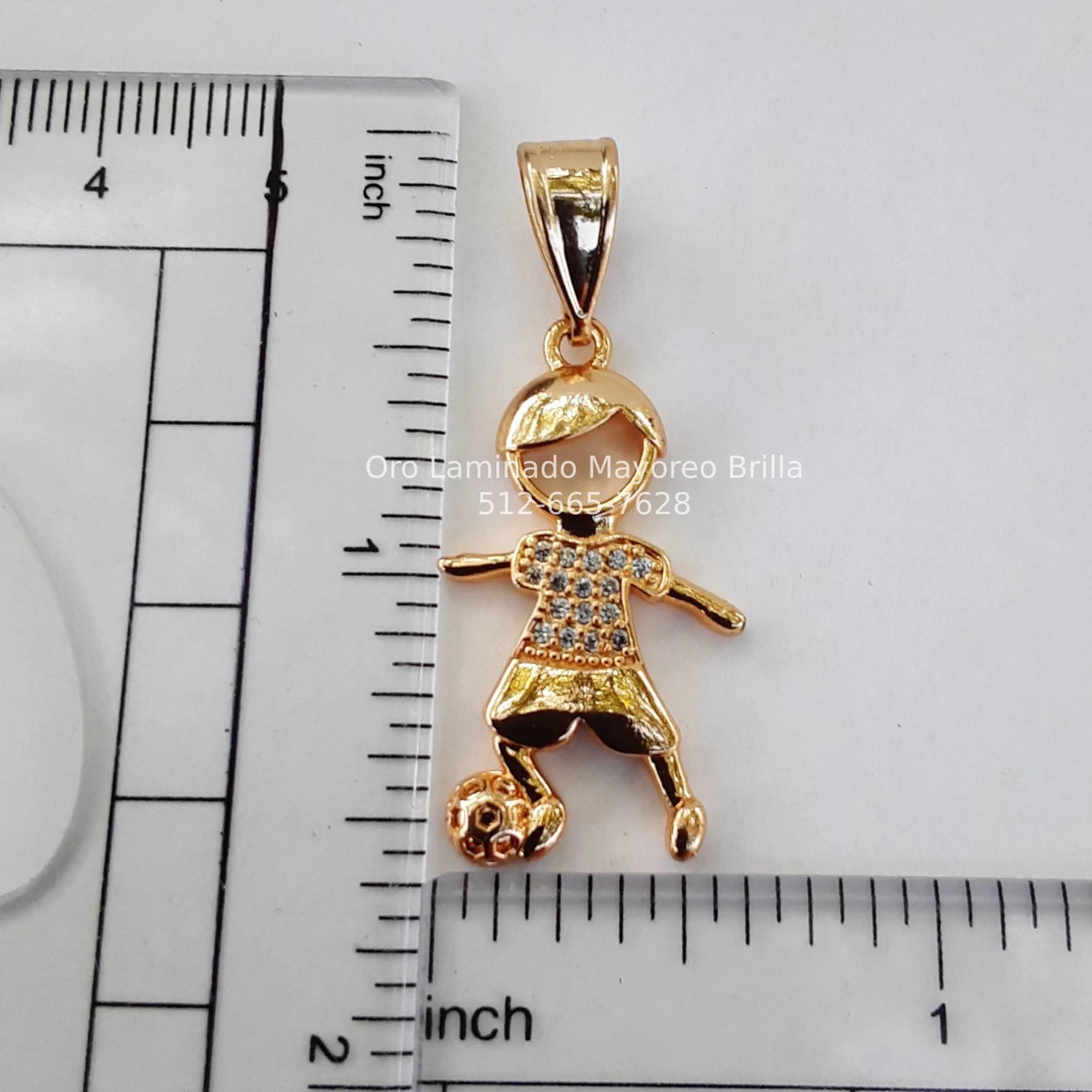 "Dije de oro laminado con diseño de niño futbolista y zirconias en la camiseta." "Laminated gold pendant featuring a soccer boy design with zirconias on the jersey."