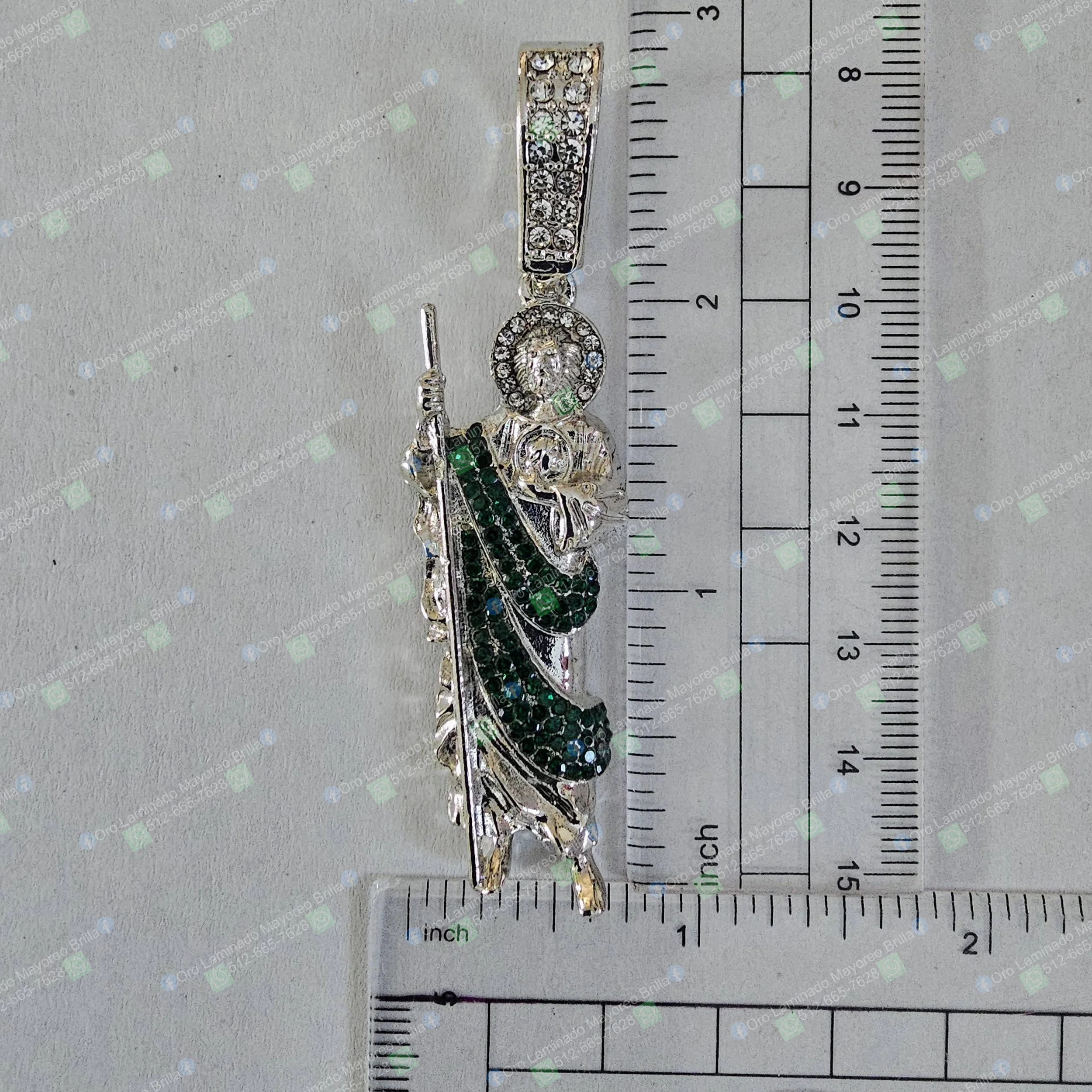 Dije religioso color plata con bastón y piedras decorativas verdes visibles | Silver color religious saint pendant with staff and visible green decorative stones