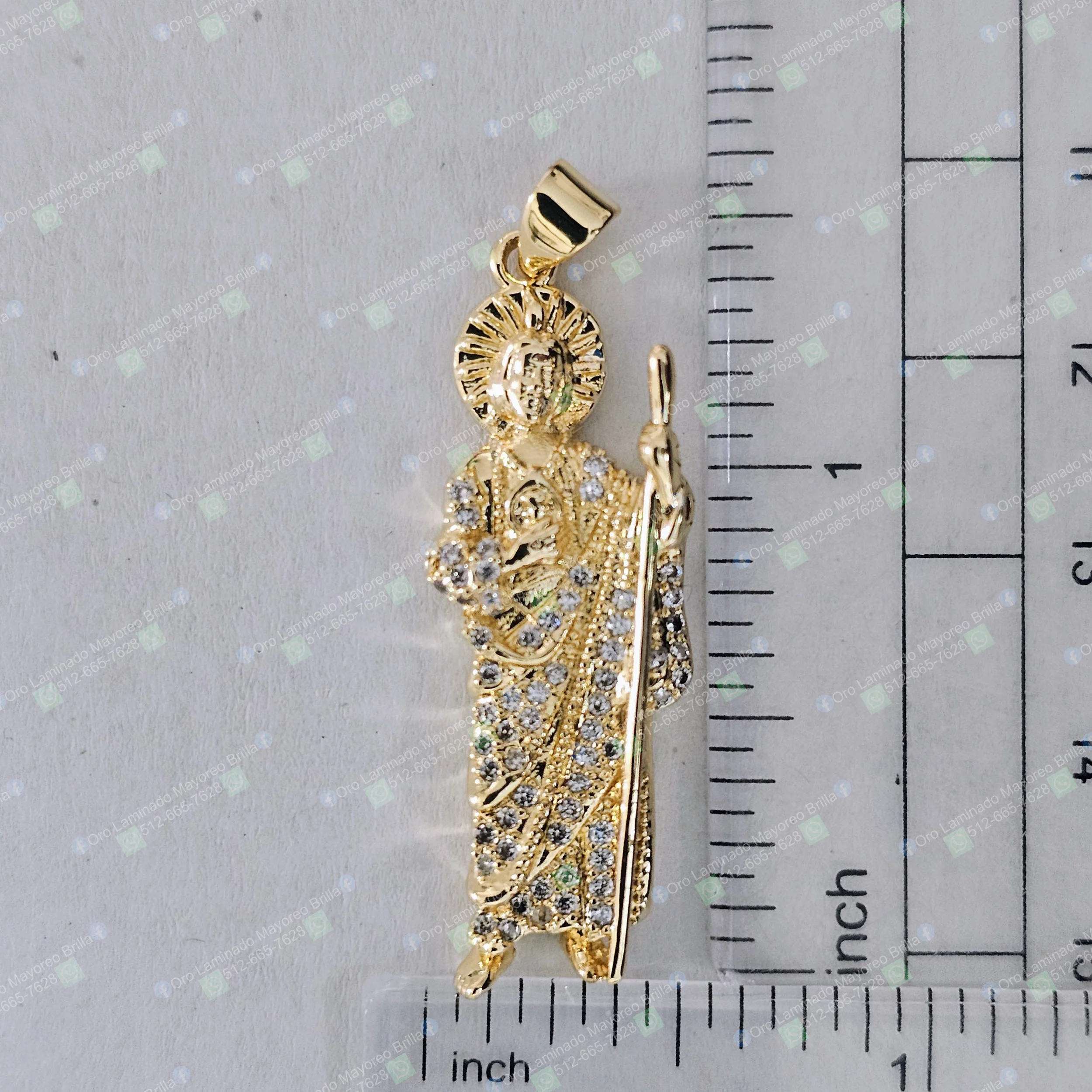 Dije religioso color oro con figura de santo, halo y piedras decorativas visibles | Gold color religious pendant with saint figure, halo, and visible decorative stones