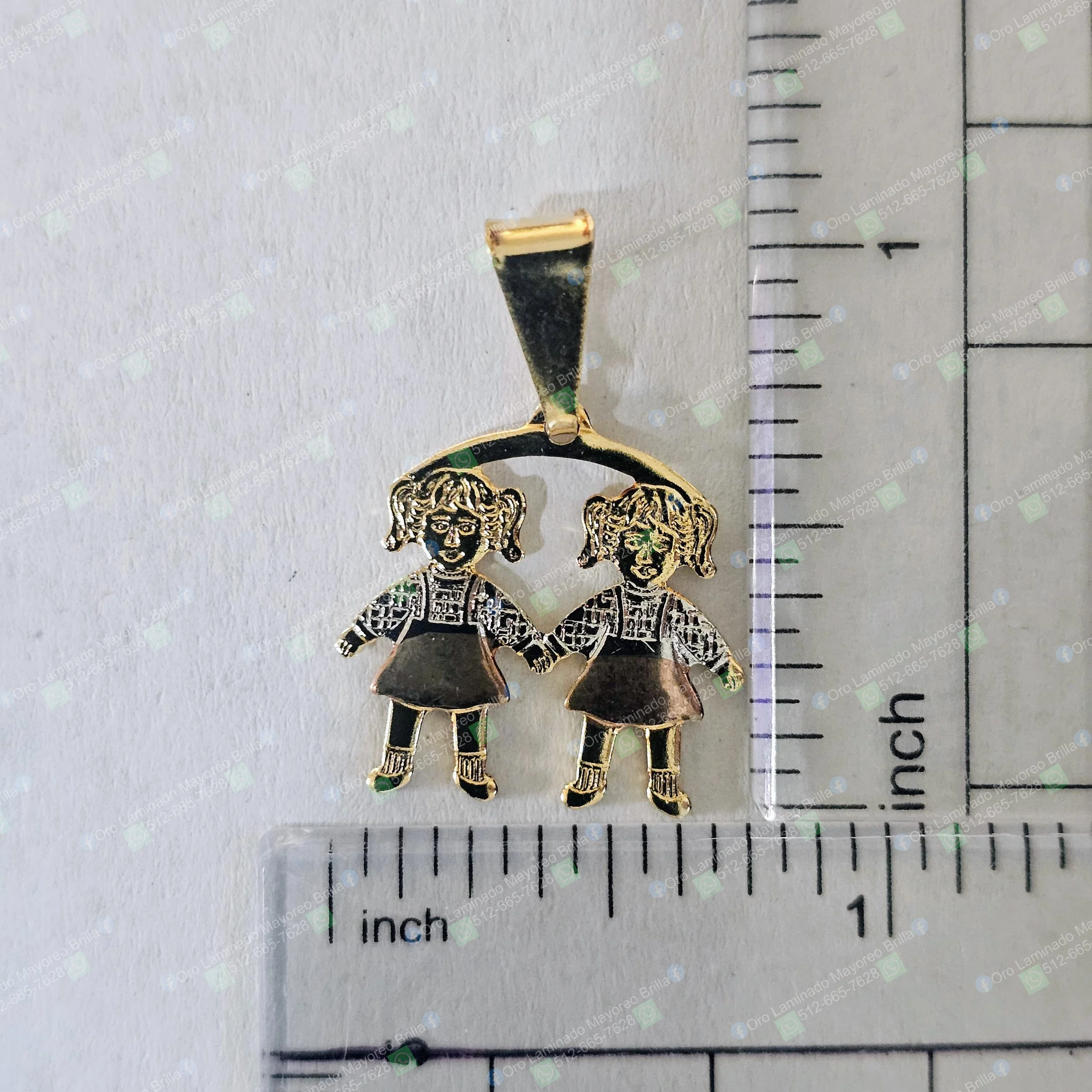 Dije color oro con dos niñas tomadas de la mano y detalles grabados visibles | Gold color pendant with two girls holding hands and visible engraved details