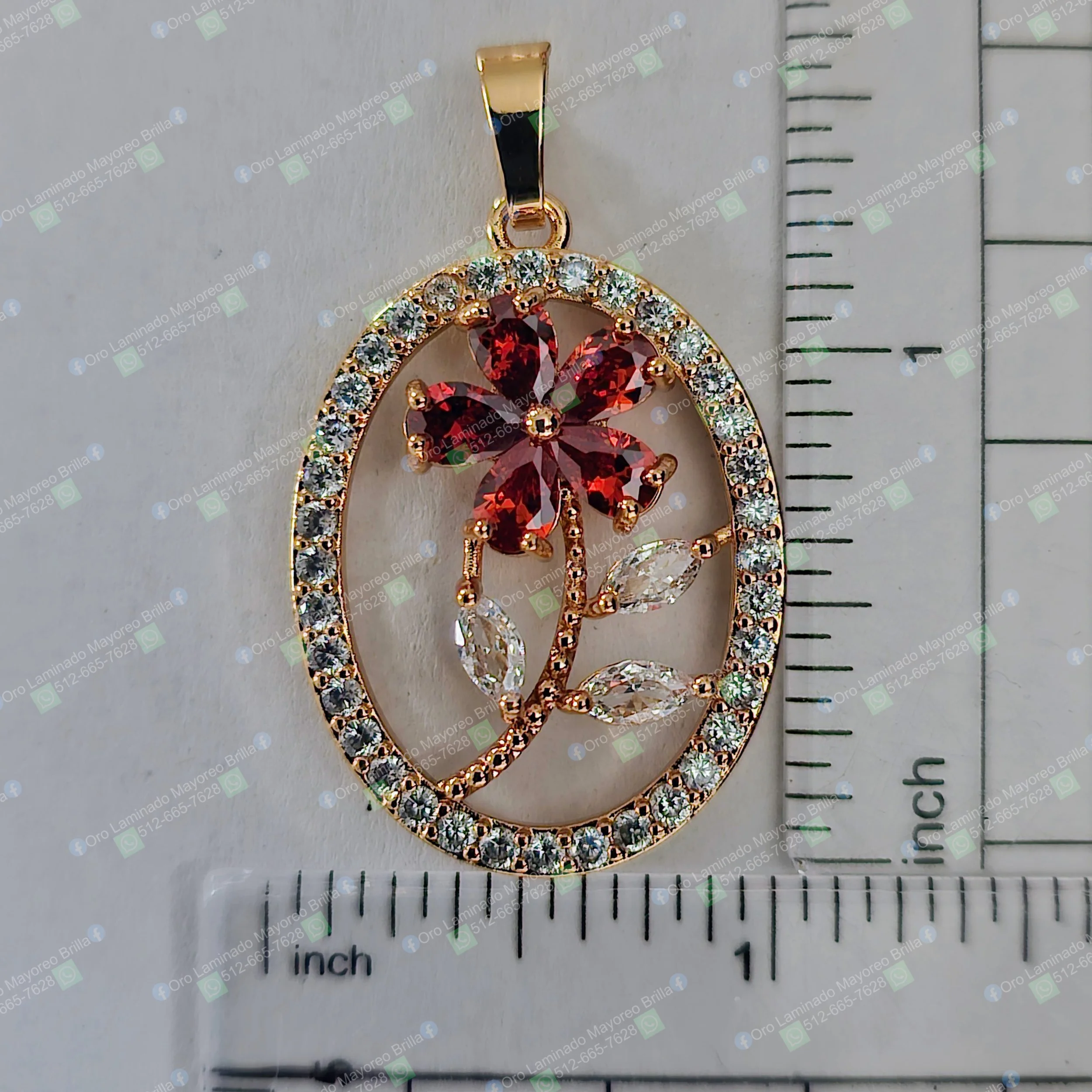 Dije ovalado color oro con flor y piedras rojas y claras visibles | Oval gold color flower pendant with visible red and clear stones