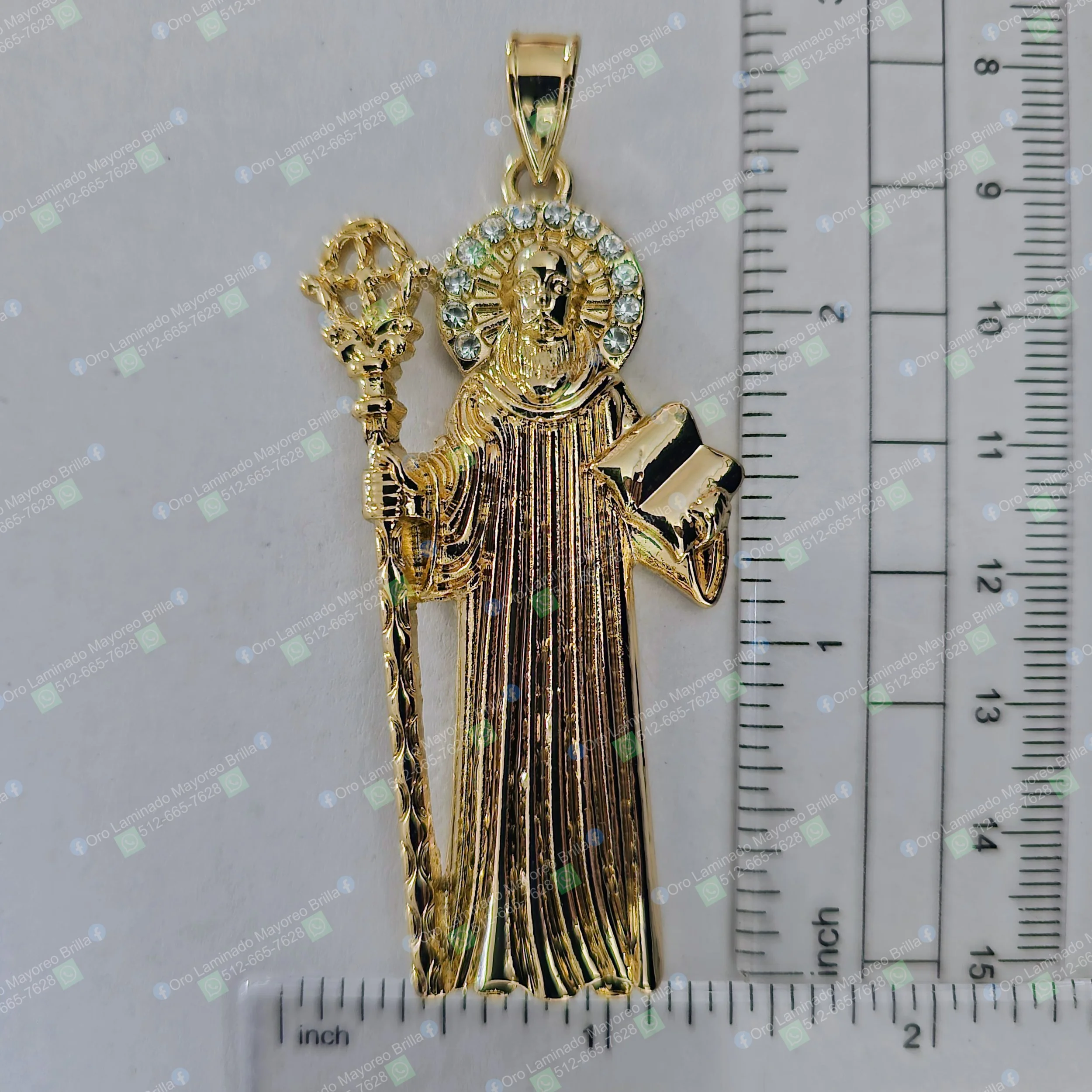 Dije de santo color oro con bastón, libro y piedras decorativas visibles | Gold color saint pendant with staff, book, and visible decorative stones