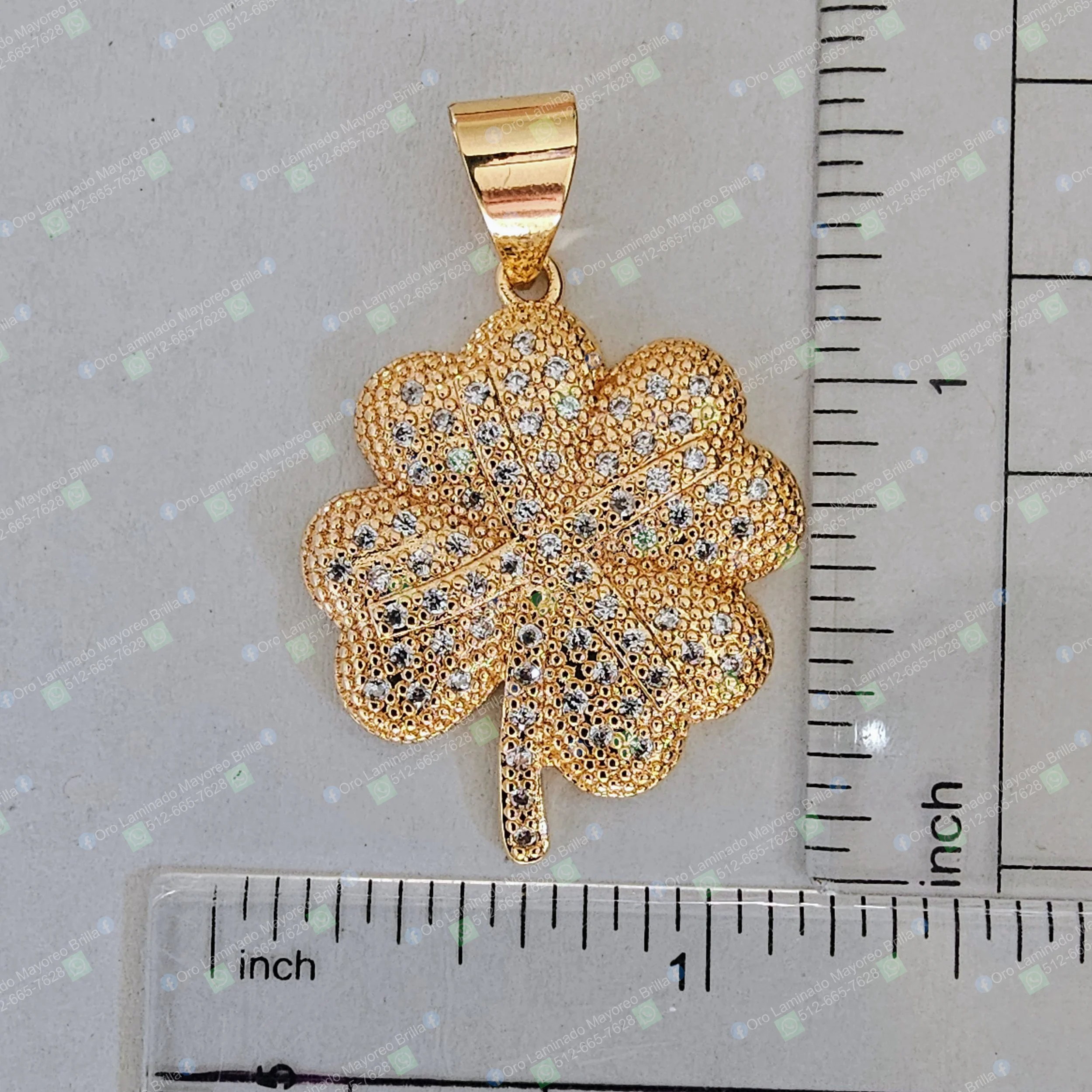 Dije de trébol de cuatro hojas color oro con piedras decorativas visibles y diseño texturizado | Gold color four-leaf clover pendant with visible decorative stones and textured design