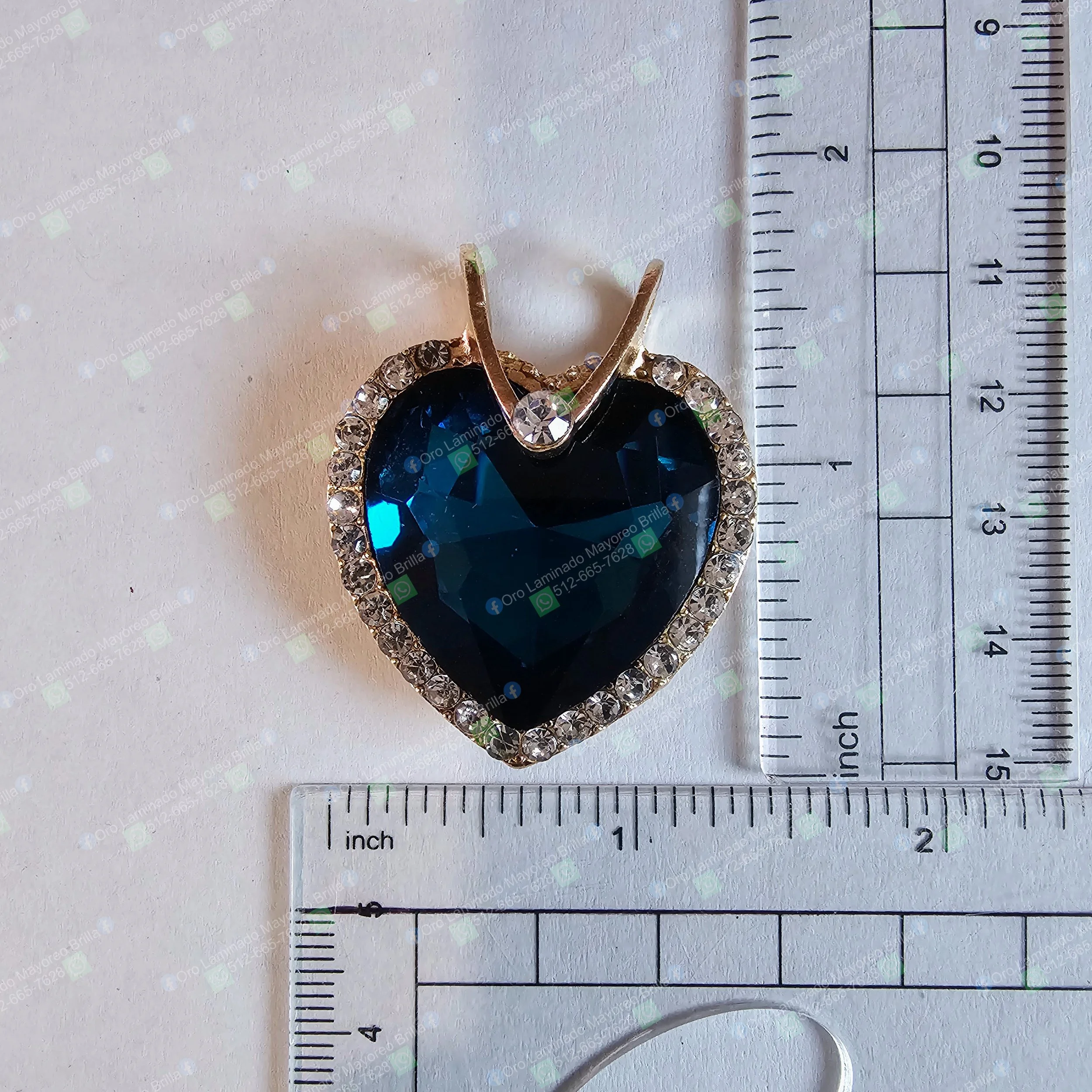 Dije de corazon color oro con piedra azul facetada y cristales decorativos visibles | Gold color heart pendant with blue faceted stone and visible decorative rhinestones