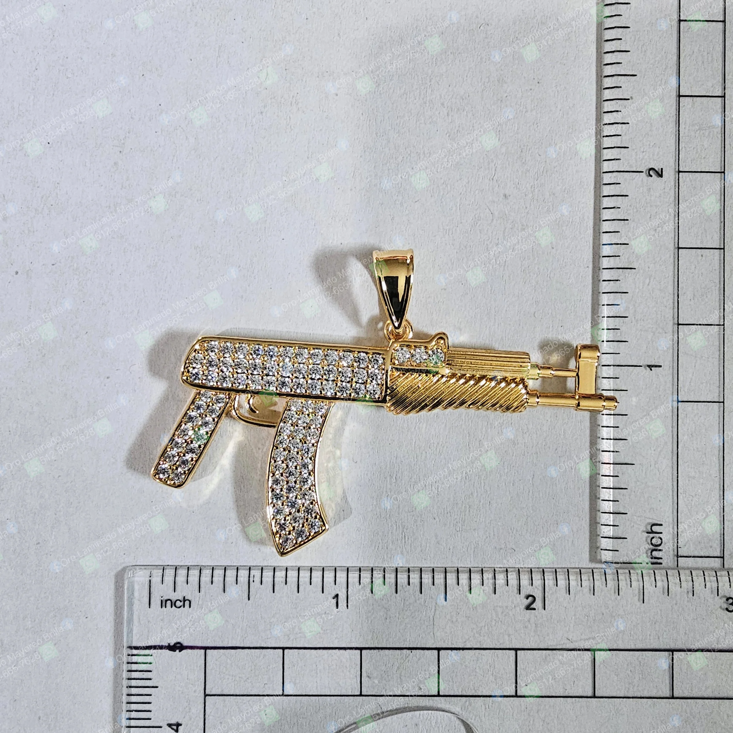 Dije de rifle color oro con piedras decorativas visibles en silueta de rifle | Gold color rifle pendant with visible decorative stones in rifle silhouette