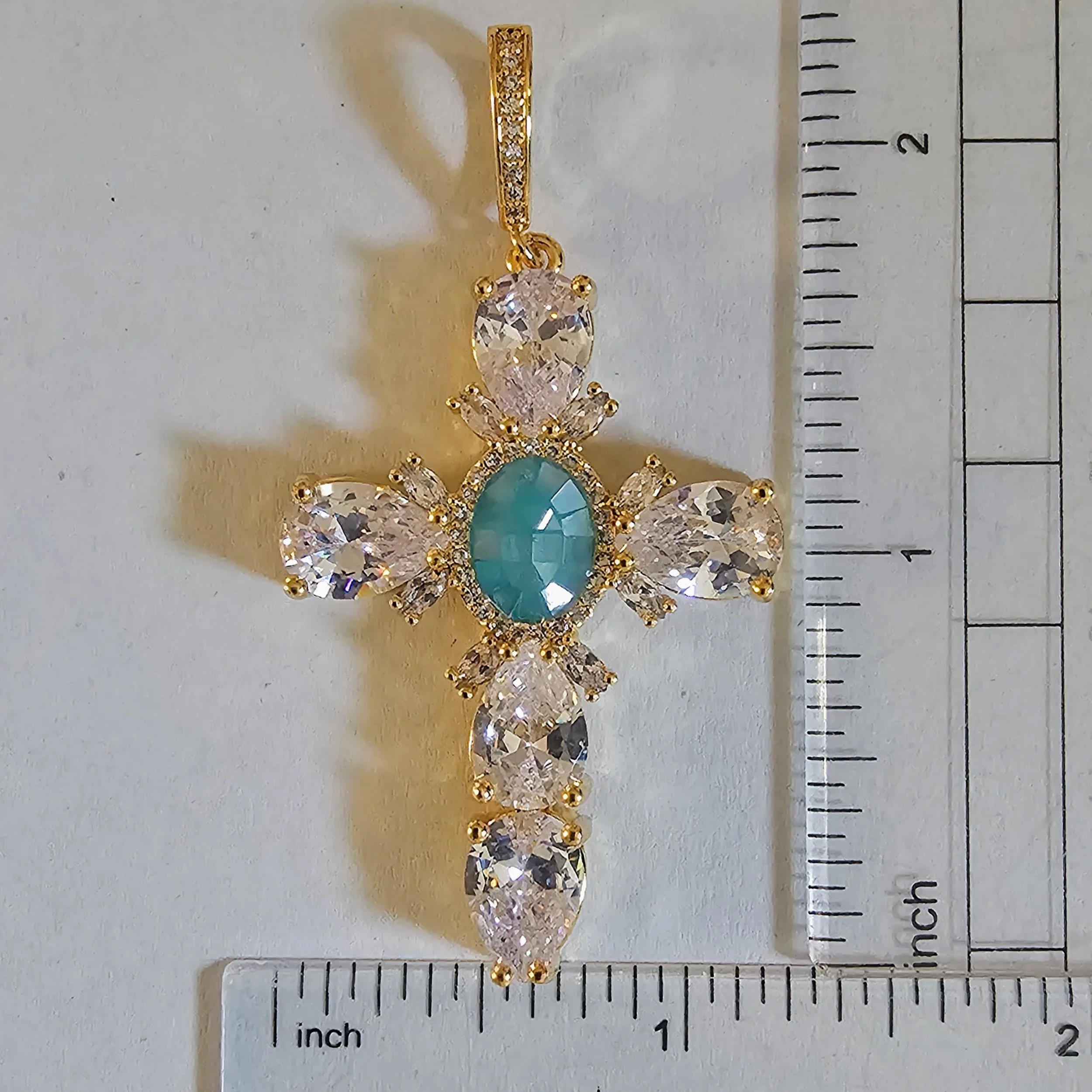 Dije de cruz color oro con piedras decorativas claras y piedra central | Gold color cross pendant with clear decorative stones and central blue