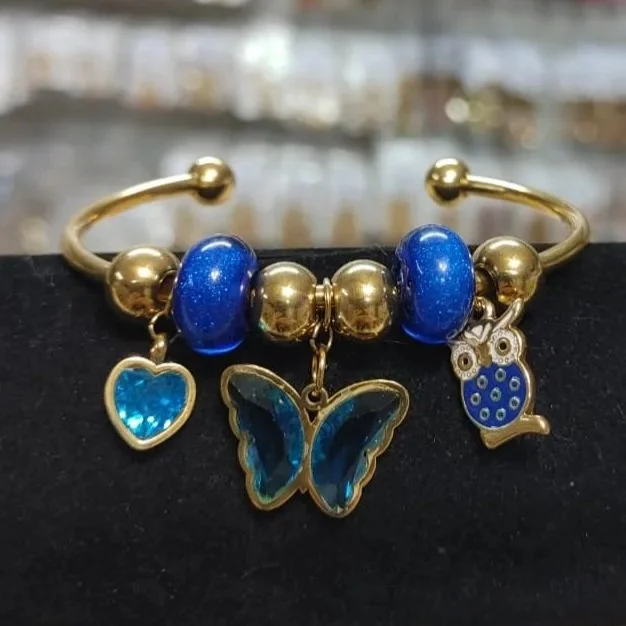 Pulsera azul con dijes de mariposa, corazón y búho en acero inoxidable. Blue bracelet with butterfly, heart, and owl charms in stainless steel.