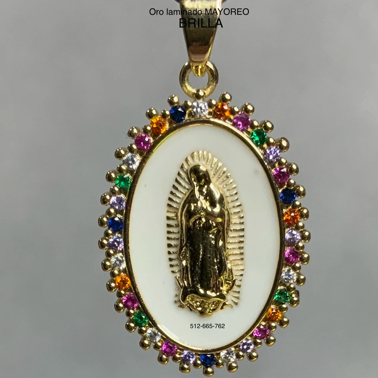 Dije ovalado con la Virgen de Guadalupe en relieve, fondo blanco y marco con piedras multicolor. Guadalupe pendant with white enamel and rainbow stones.