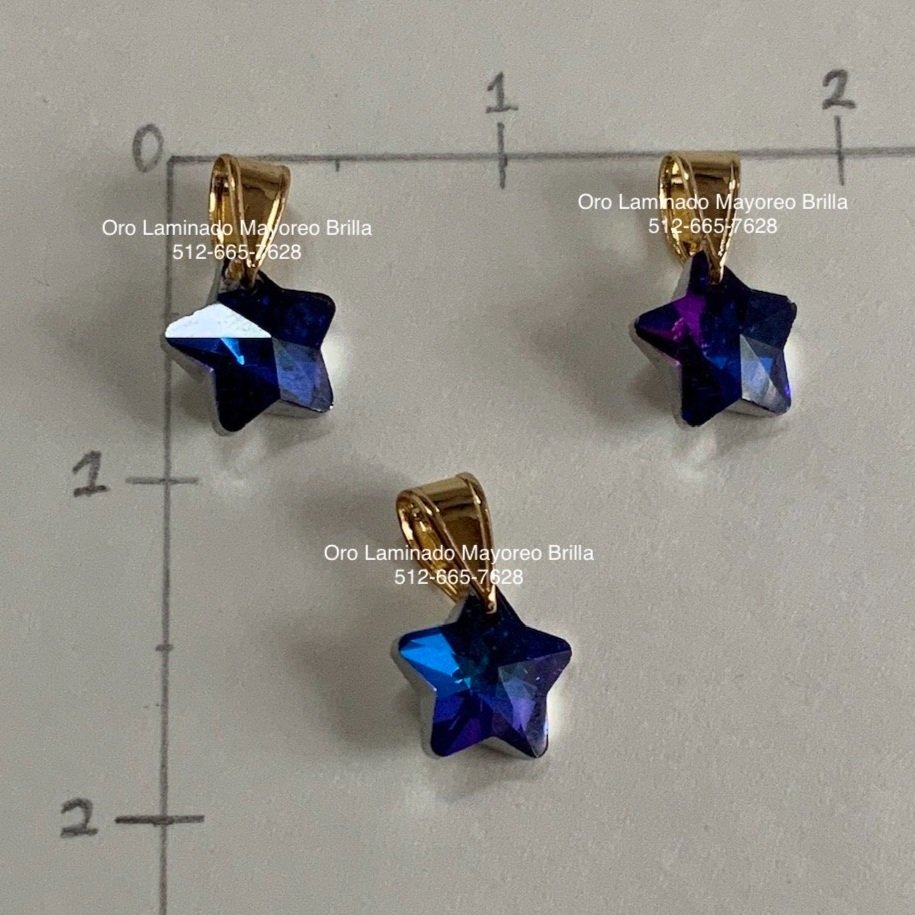"Paquete de 3 dijes de oro laminado en forma de estrella con cristales azul tornasol." "3-pack of laminated gold star-shaped charms with iridescent blue crystals."