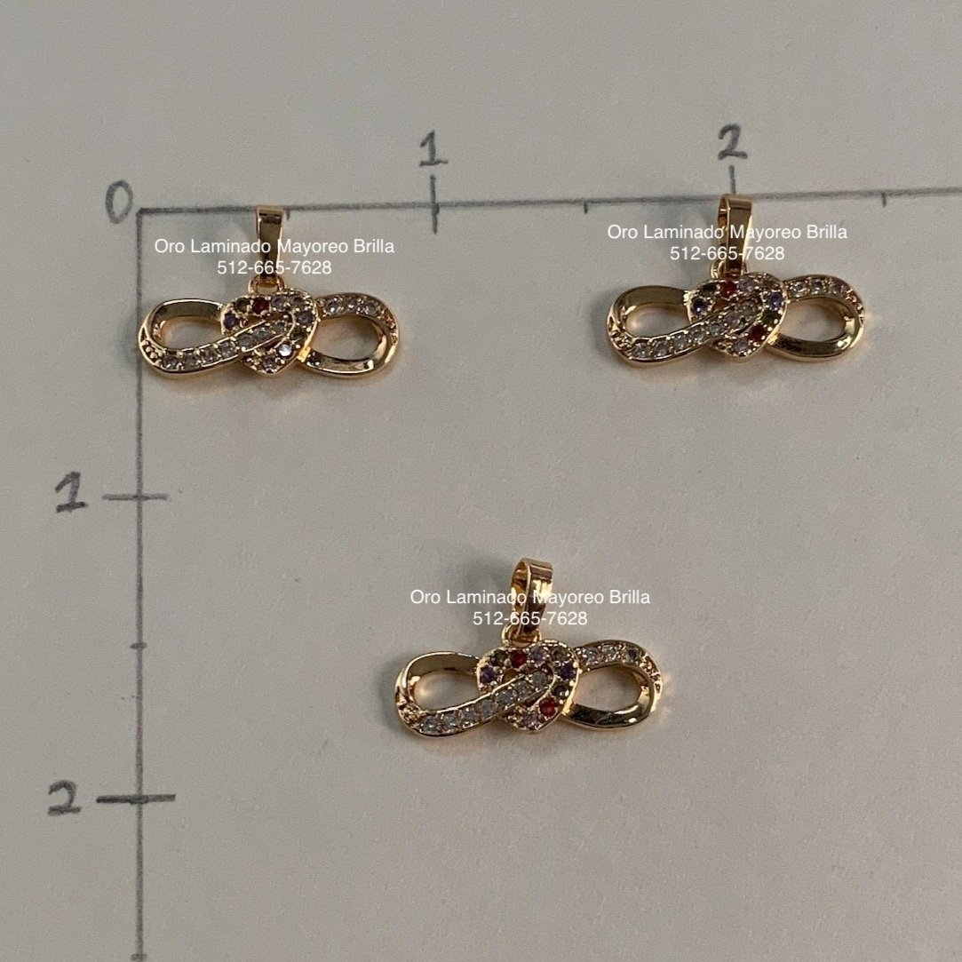 "Paquete de 3 dijes de oro laminado con diseño de infinito y cristales brillantes." "3-pack of laminated gold infinity-shaped charms with sparkling crystals."