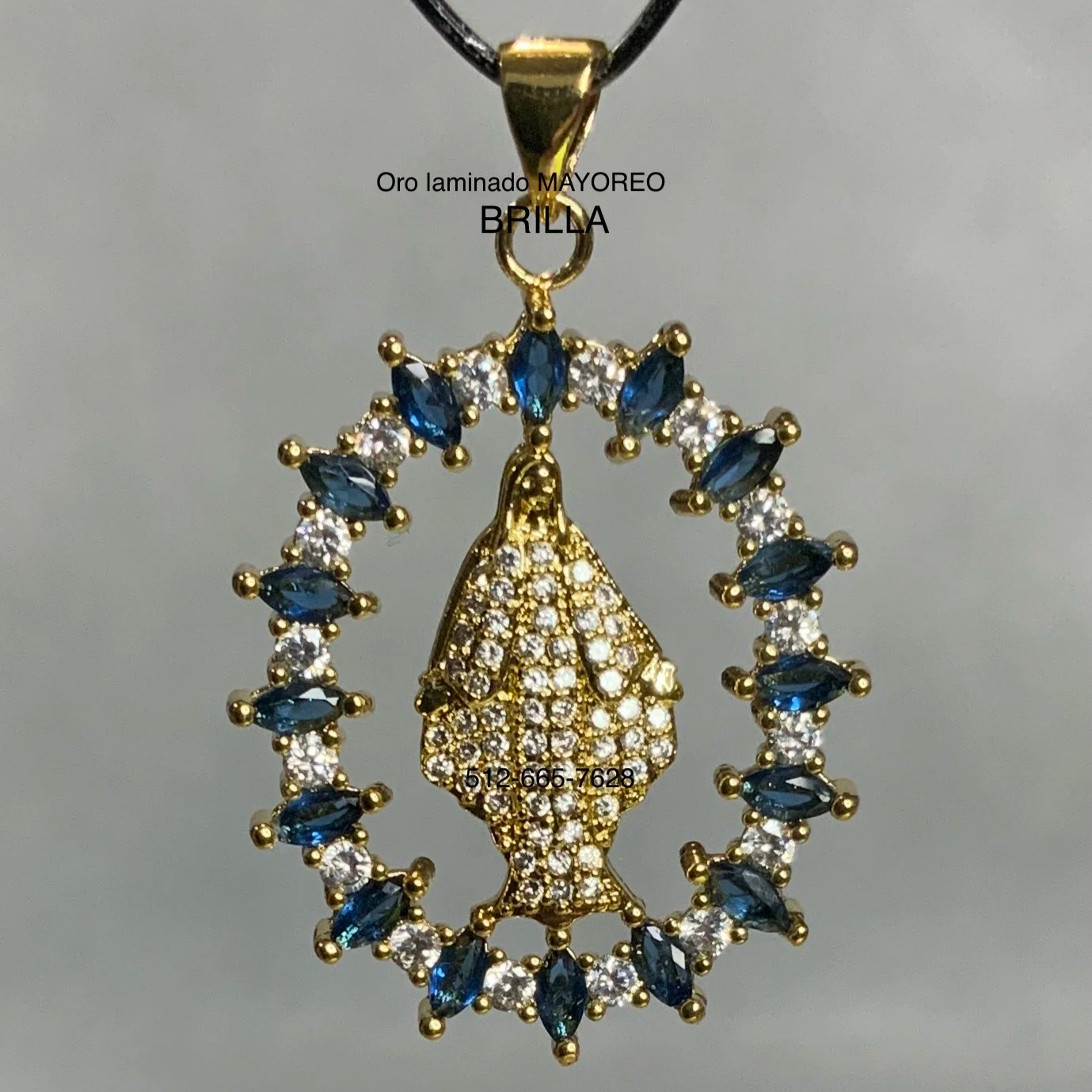 Dije dorado con figura de la Virgen incrustada y borde circular de piedras azul zafiro. Gold pendant Virgin Mary with blue and white zircon halo.