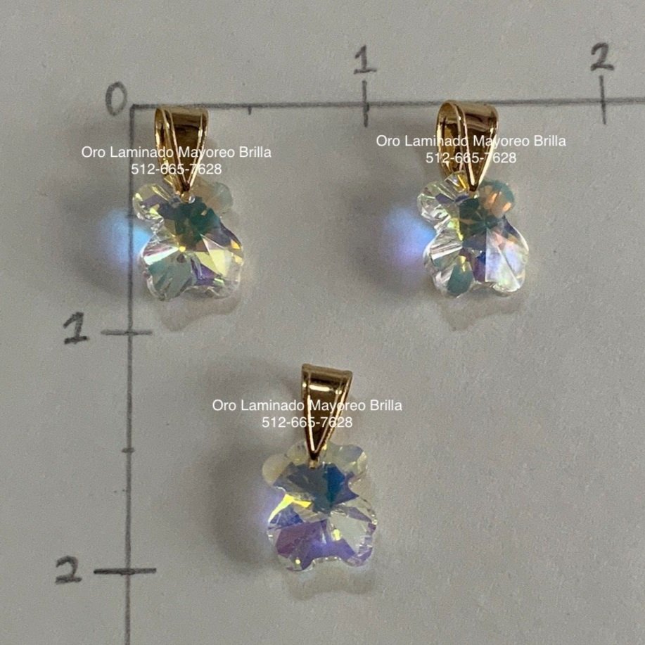 "Paquete de 3 dijes de oro laminado en forma de osito con cristales transparentes tornasol." "3-pack of laminated gold bear-shaped charms with transparent iridescent crystals."