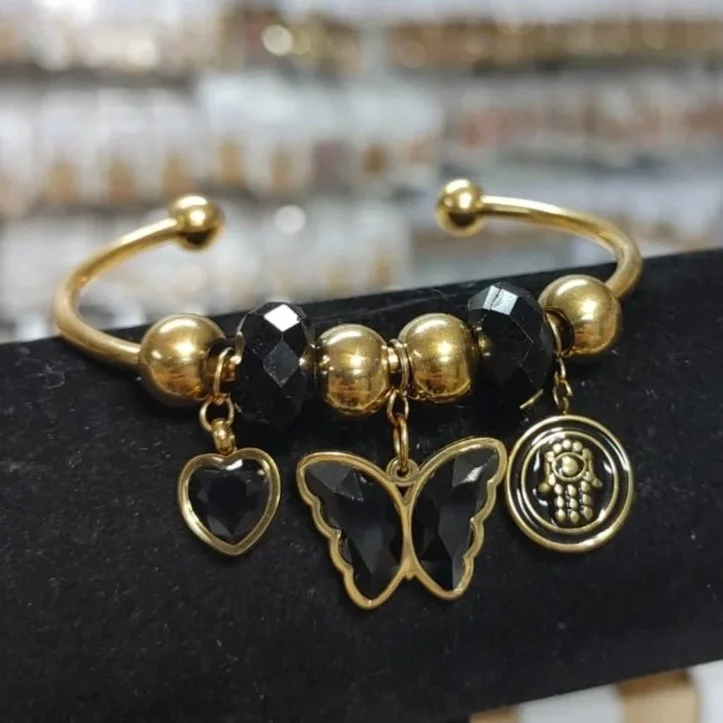 Pulsera negra con mariposa, corazón y medalla religiosa en acero inoxidable. Black bracelet with butterfly, heart, and religious charm in stainless steel.
