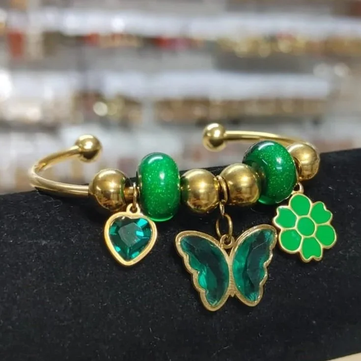 Pulsera verde con mariposa, corazón y flor de la suerte en acero inoxidable. Green bracelet with butterfly, heart, and lucky flower charms in stainless steel.