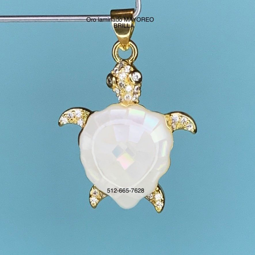 Dije de tortuga en oro laminado con concha blanca brillante. Gold-plated turtle pendant with shimmering white shell.