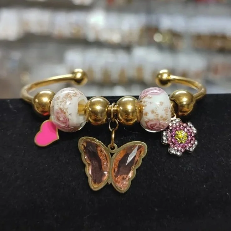 Pulsera con dijes de mariposa, corazón y flor en acero inoxidable. Bracelet with butterfly, heart, and flower charms in stainless steel.