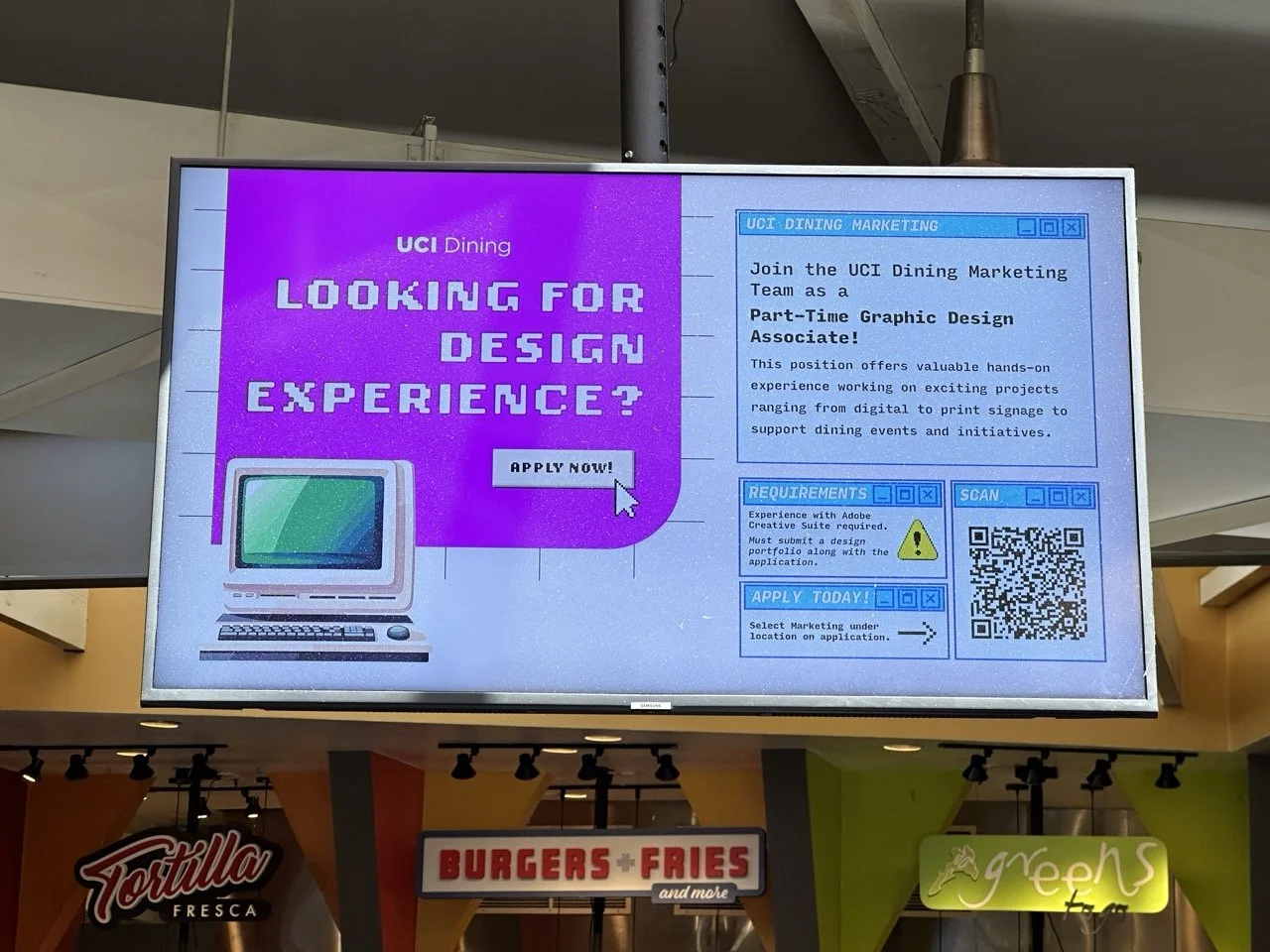 Digital display advertising a part-time graphic design position with UCI Dining, featuring a pixelated computer graphic on a purple background and blue sections with job requirements and apply instructions.